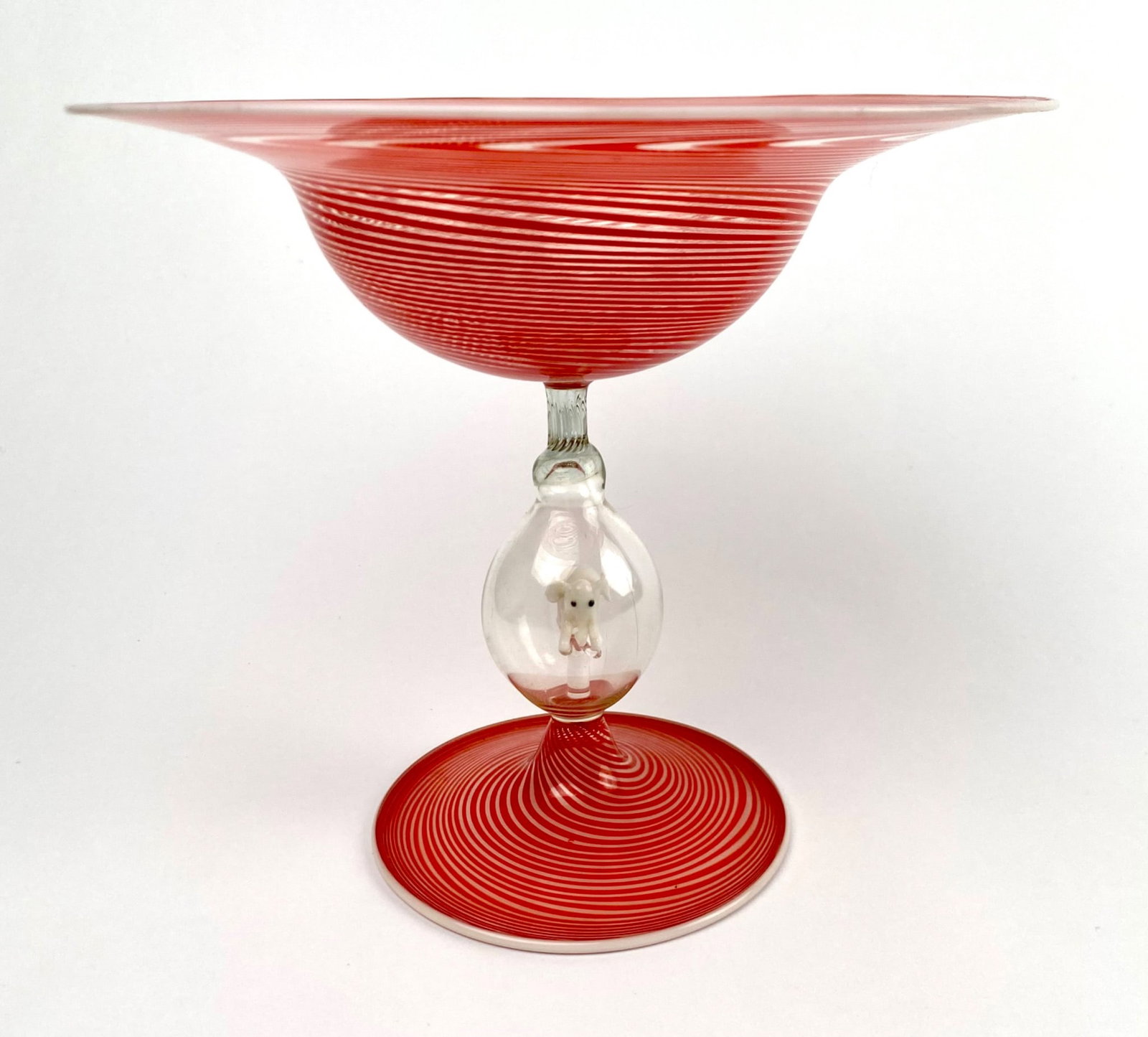Bimini Werkstatte Glass with Encased White Elephant Motif: Red swirl glass by accentuated by a clear stem containing a white elephant motif. The piece showcases intricate detailing. Item is in good condition. Please see photos for additional details. | Dimens
