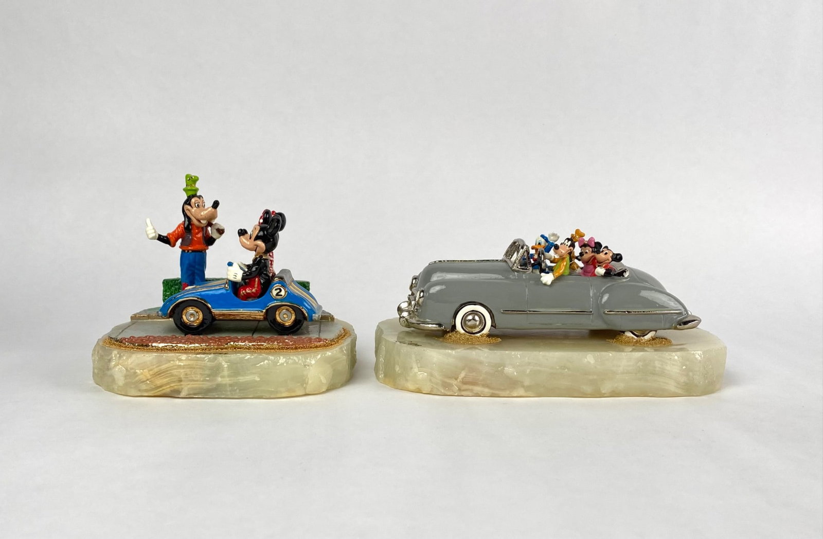 Pair of Ron Lee Disney Figurines : Pair of Disney collectible figurines, each mounted on stone bases. One depicts Mickey, Minnie, and Goofy with a blue car signed and numbered 292/750. The other features Mickey, Minnie, Goofy, and Dona