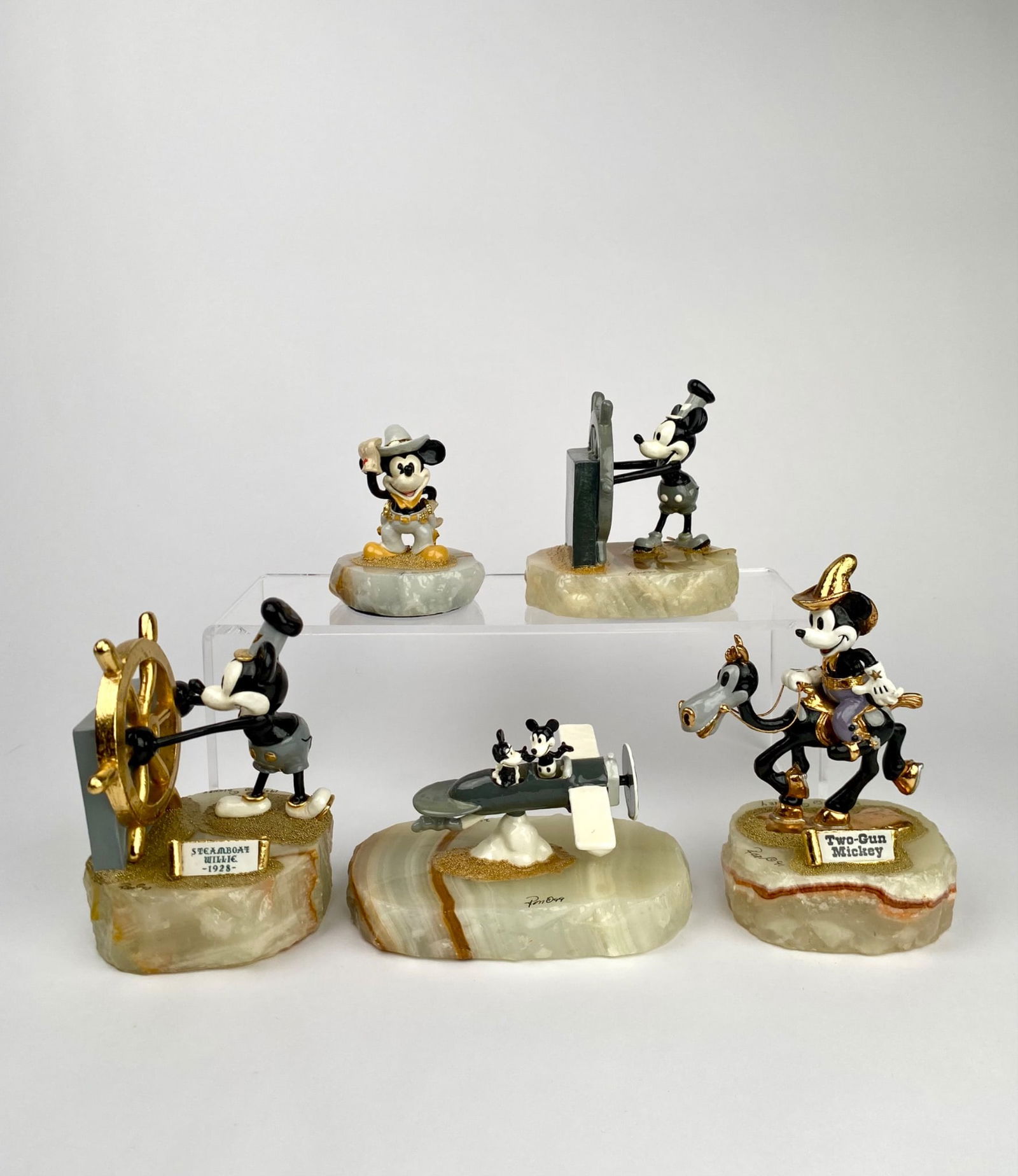 Set of Five Ron Lee Disney Mickey Mouse Figurines: Set of five Disney-themed Mickey Mouse figurines, each depicted in unique scenes and mounted on onyx bases. Includes Steamboat Willie, Two-Gun Mickey, a plane ride scene, and other moments of classic