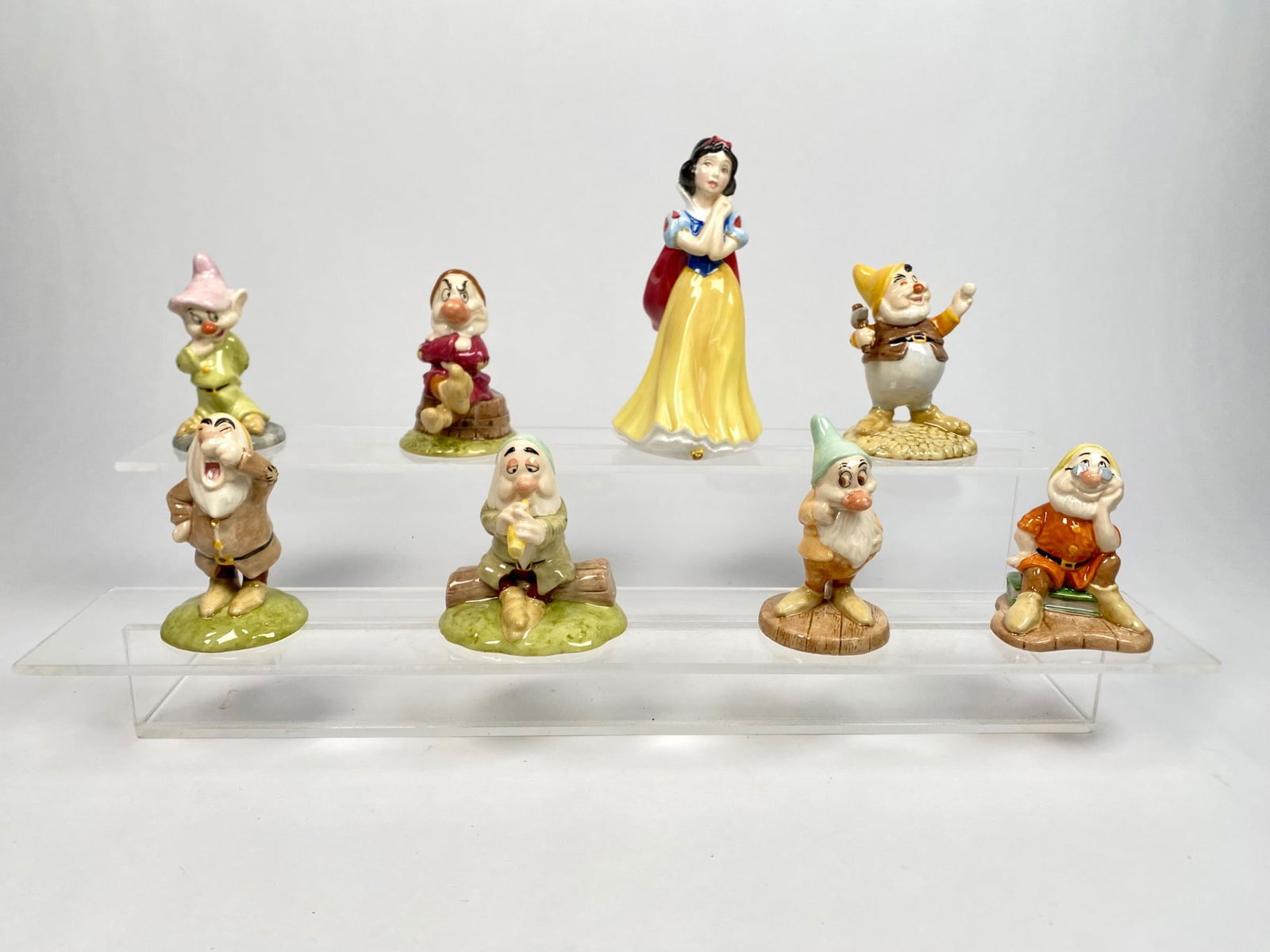 Royal Doulton Disney Snow White and Seven Dwarfs Figurines Set: Set of Royal Doulton figurines featuring Snow White and the Seven Dwarfs, marked on the bases with company branding and Disney partnership. Each figurine is crafted in porcelain and hand-painted. The