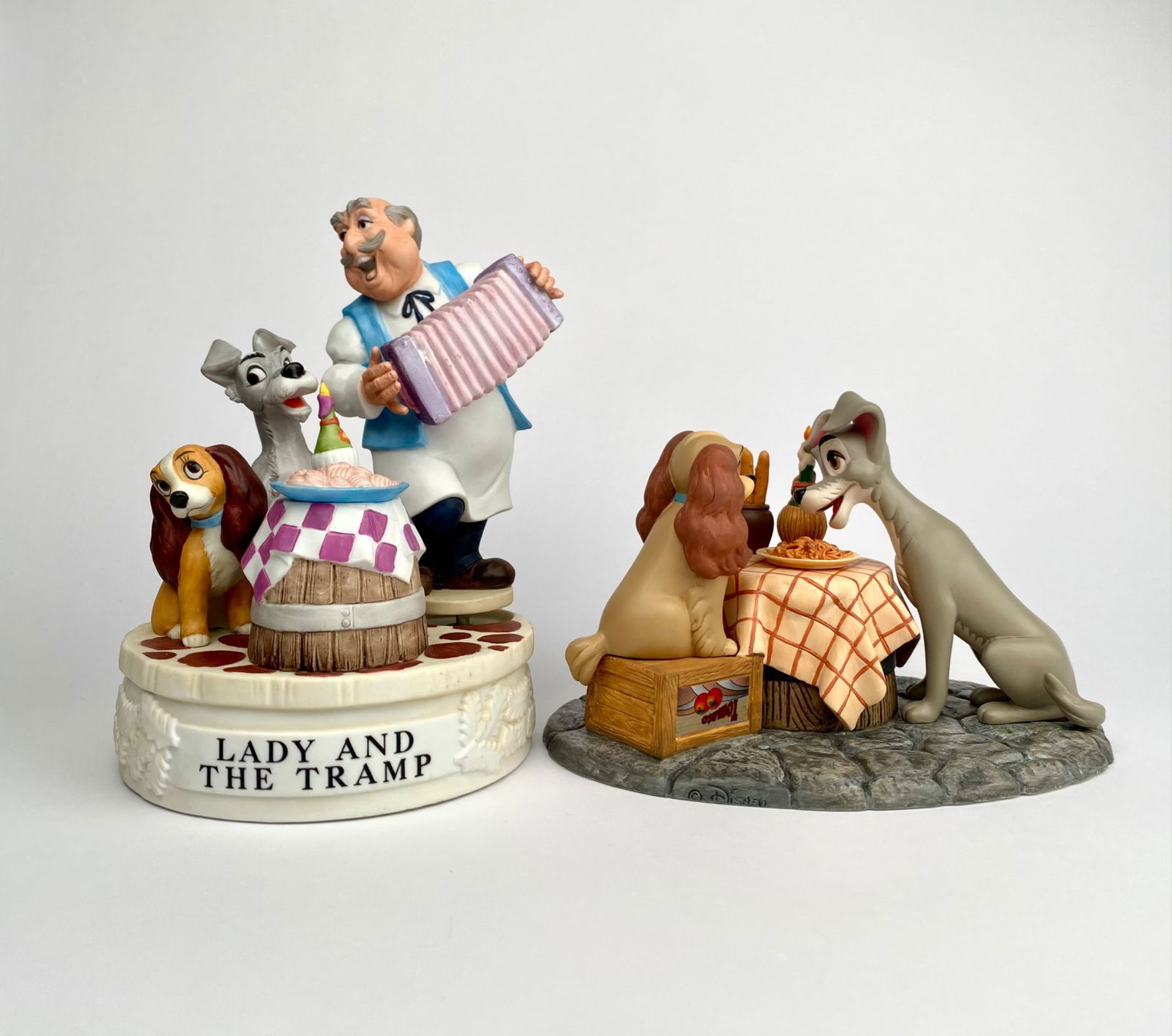 Pair of Disney Lady and the Tramp Musical Figurines: Two Disney Lady and the Tramp collectible items. The first is a display scene featuring Lady and Tramp sharing a spaghetti dinner, crafted with realistic details on a cobblestone base. The second is a