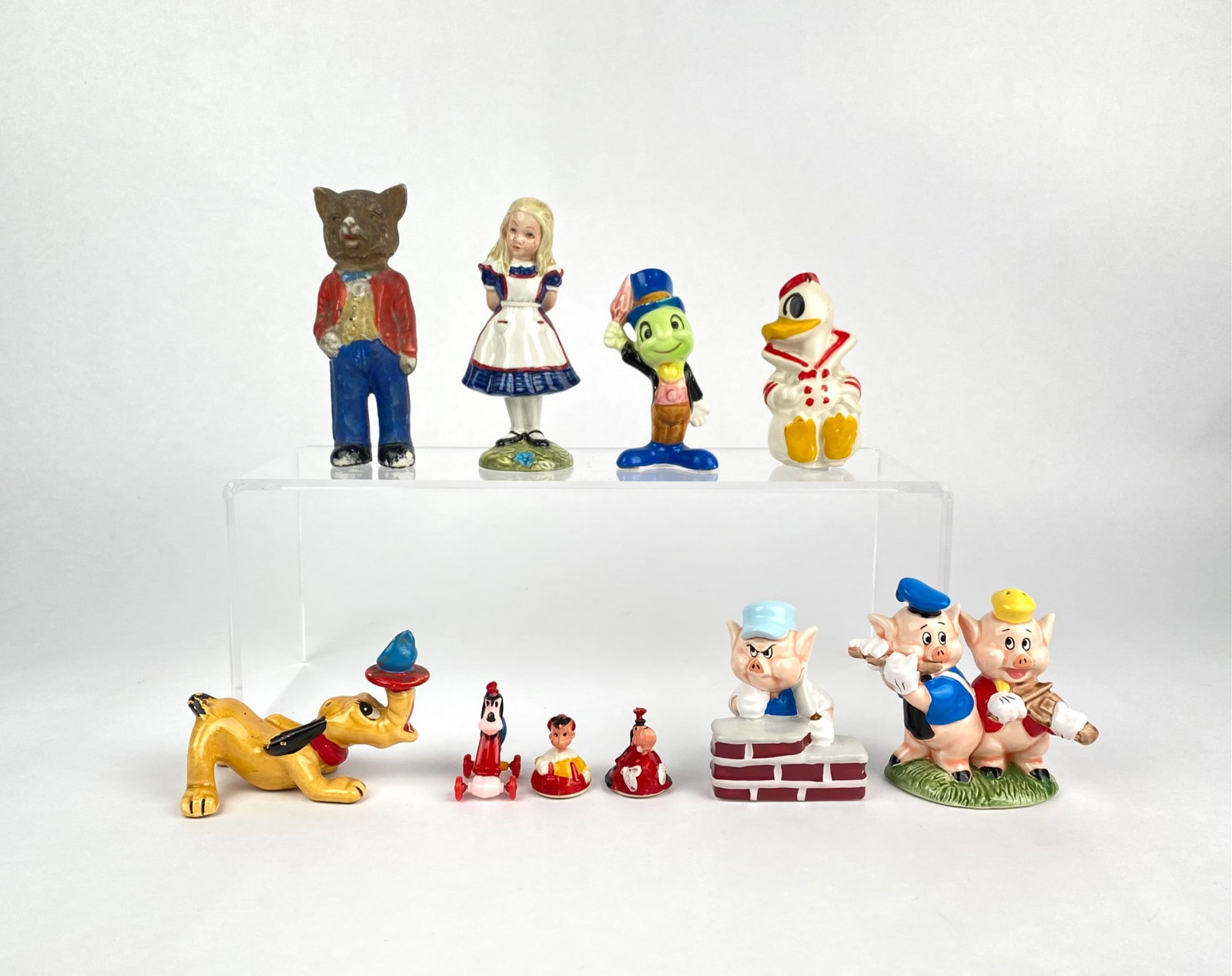 Collection of Hand Painted Disney Figurines: A collection of hand painted figurines featuring iconic characters, including Alice from Alice in Wonderland, Pluto, Donald Duck, Jiminy Cricket, the Three Little Pigs, Goofy, and others. Each figure 