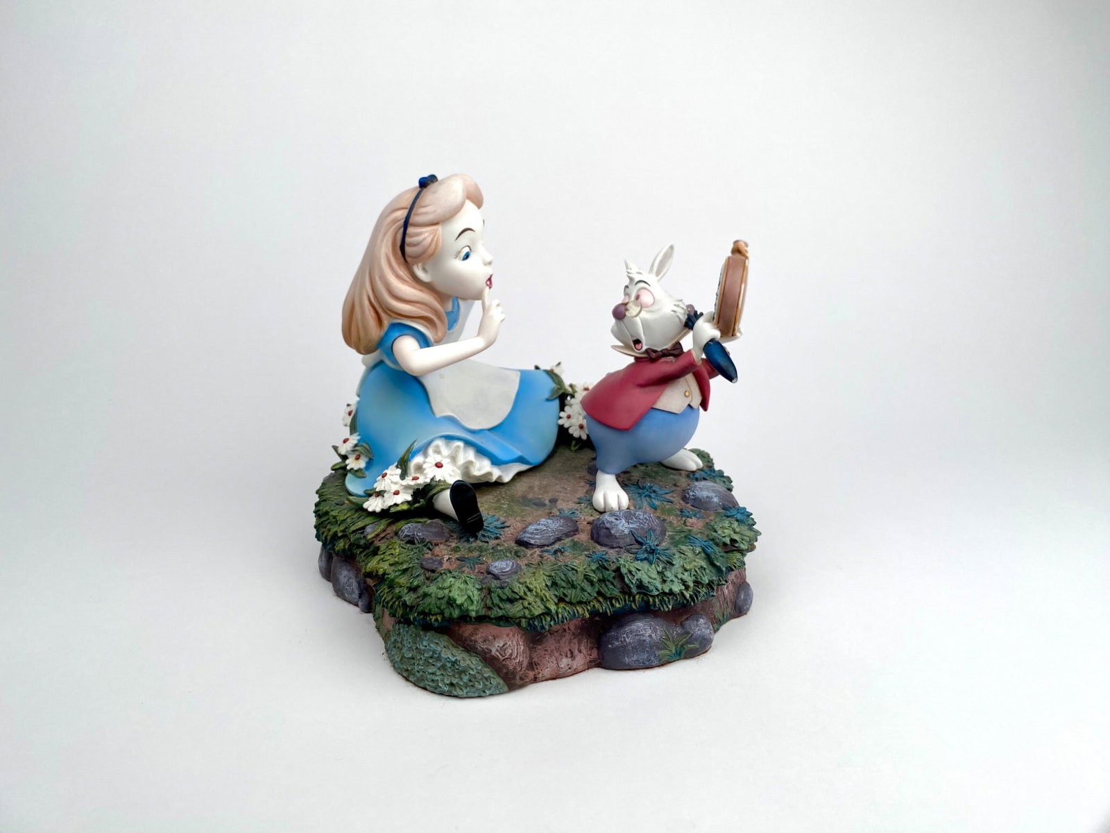 Disney 2000 Alice and White Rabbit Figurine by Markrit: Disney figurine depicting Alice and the White Rabbit on a scenic base, marked Disney 2000 Markrit. The piece features vibrant colors and detailed texturing, including flowers, grass, and rocky element