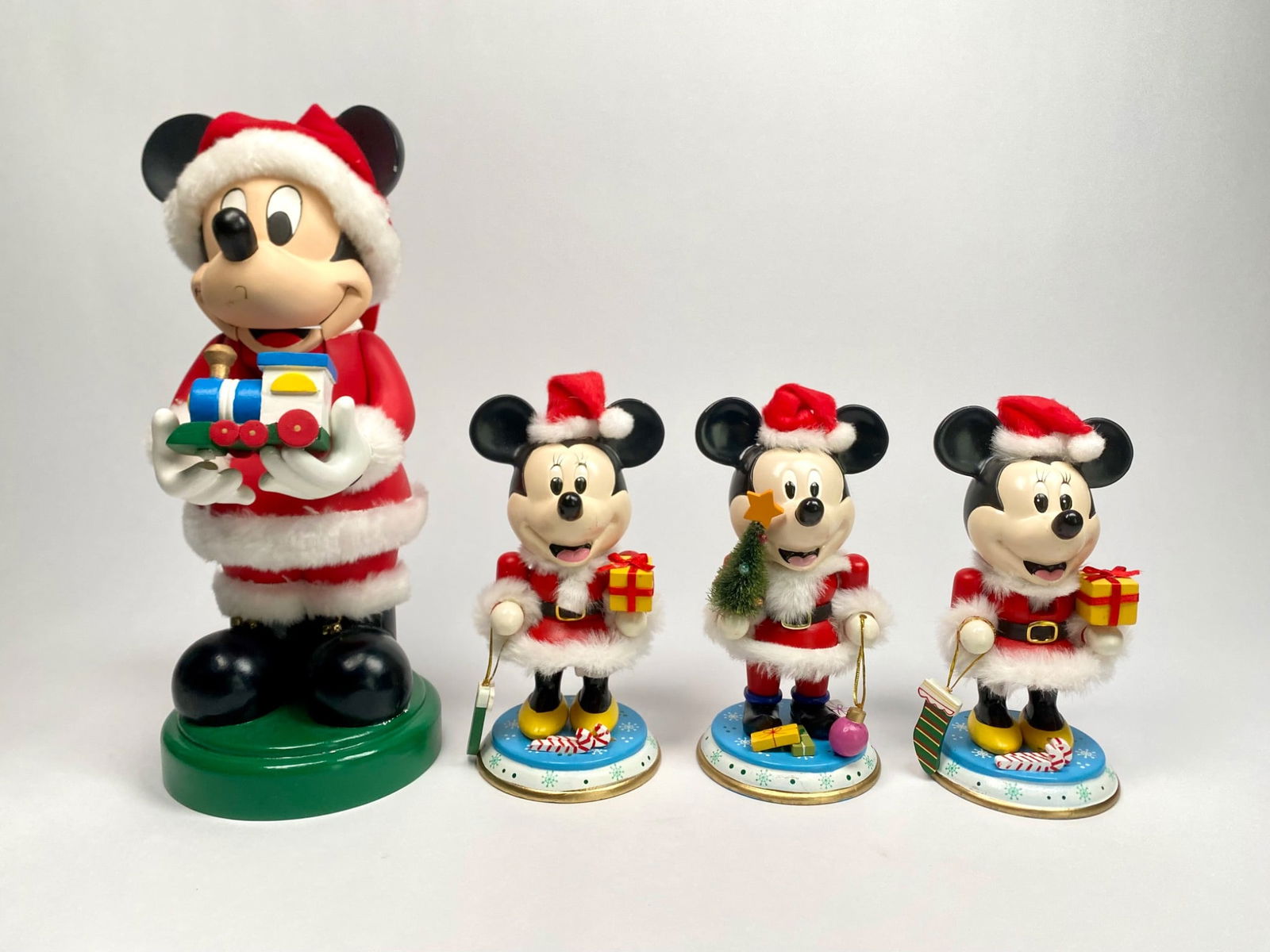 Set of Four Mickey and Minnie Mouse Christmas Nutcrackers: Set of four resin Christmas themed nutcrackers featuring Mickey and Minnie Mouse dressed in festive Santa Claus outfits, holding small gifts and holiday decorations. Includes one larger nutcrackers an
