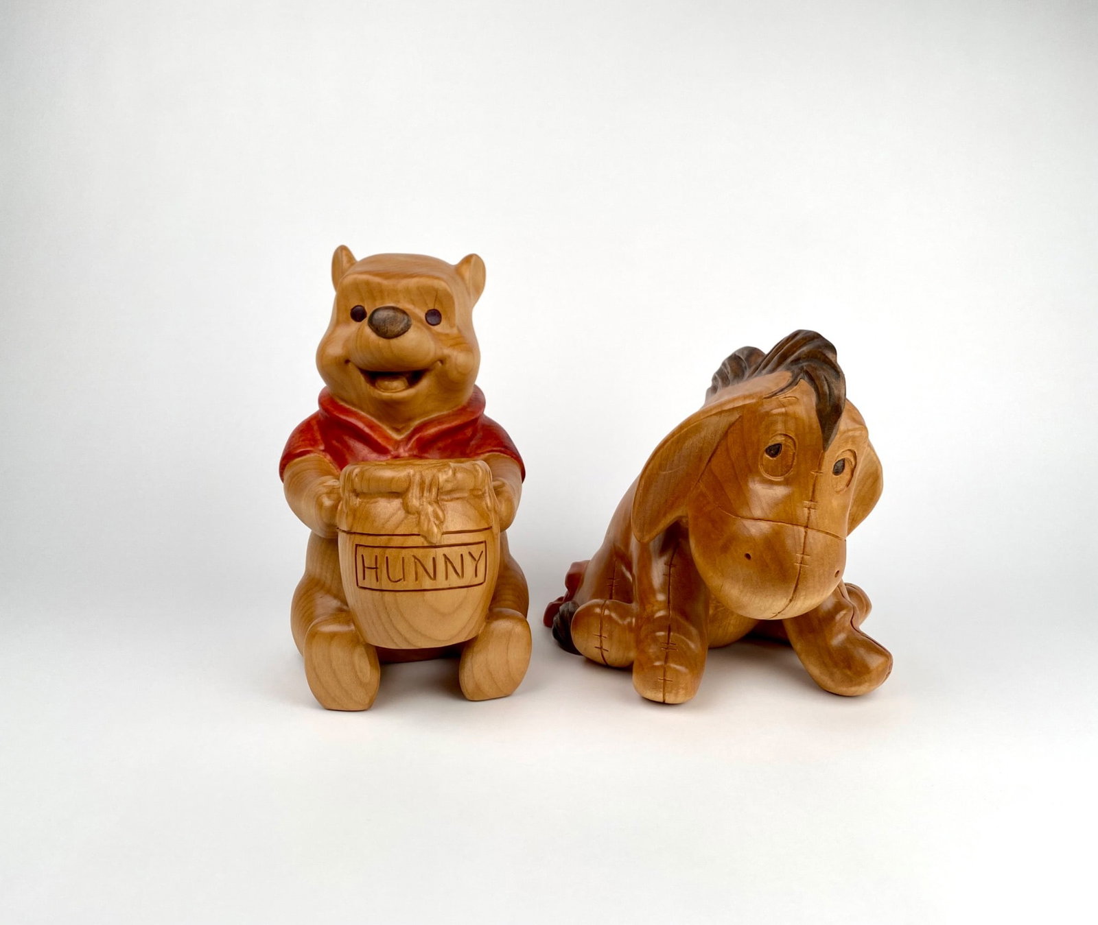 Set of 2 Large Disney Pooh and Eeyore Wooden Figurines: Set of two large wooden Disney collectible figurines featuring Winnie the Pooh and Eeyore. Pooh holds a Hunny pot while wearing a painted red shirt, and Eeyore displays stitched detailing with darker 