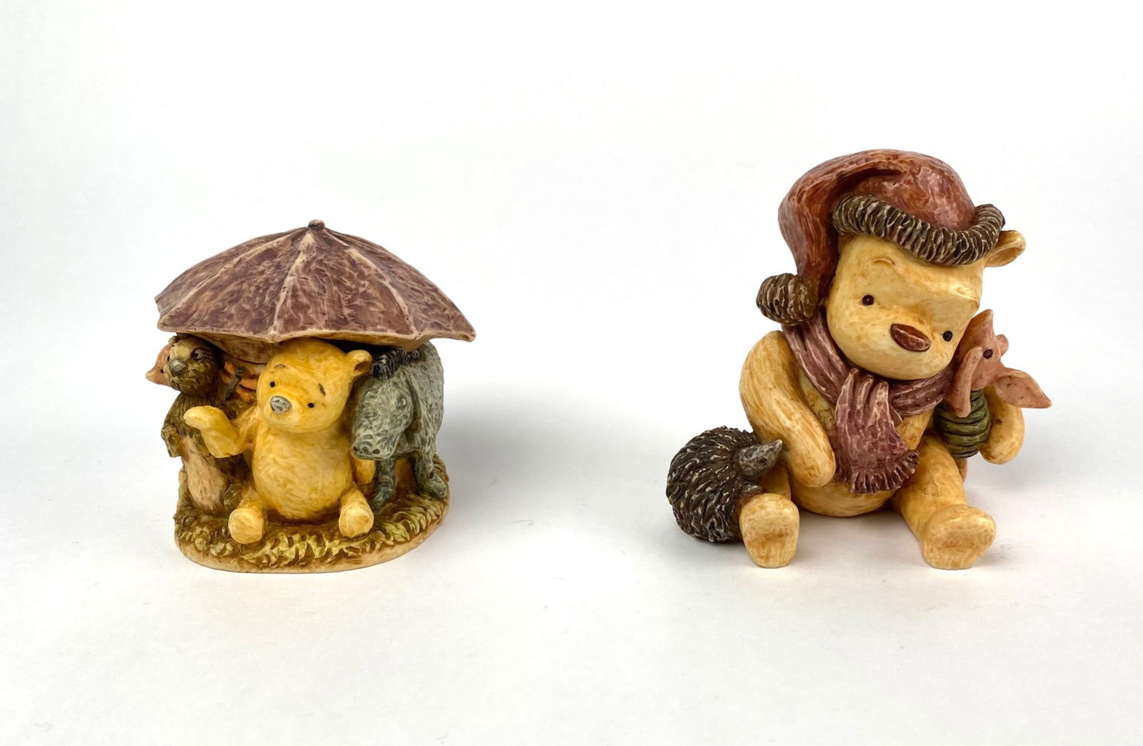 Harmony Kingdom Disney Winnie the Pooh Figurines, Set of 2: Set of two Harmony Kingdom Disney collectible figurines featuring Winnie the Pooh themes. The first figurine depicts Pooh and friends, including Piglet, Eeyore, and others, gathered under an umbrella.