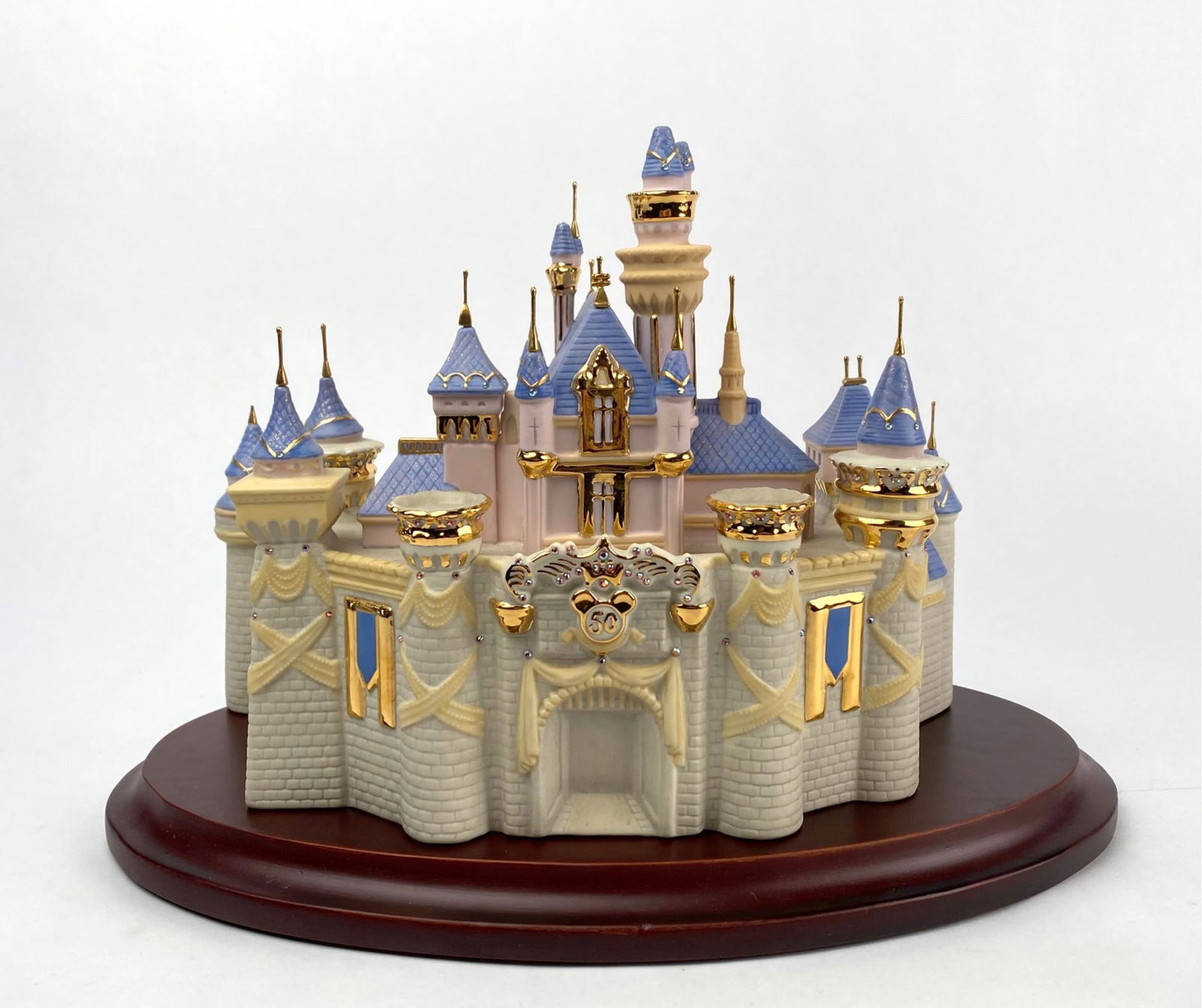 Disneyland 50th Anniversary Sleeping Beauty Castle Figurine?: Disneyland 50th Anniversary Sleeping Beauty Castle figurine with intricate design details and gold-tone accents. Made from ceramic material and mounted on an oval wooden base. Features iconic castle a