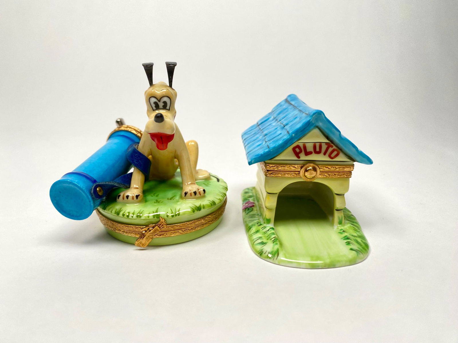 Pair of Disney Pluto Artoria Limoges Boxes: Set of two Artoria Limoges hand painted porcelain trinket boxes featuring Disneys Pluto. One piece depicts Pluto on a grassy base with an attached bag of golf clubs, opening to reveal a painted bone m