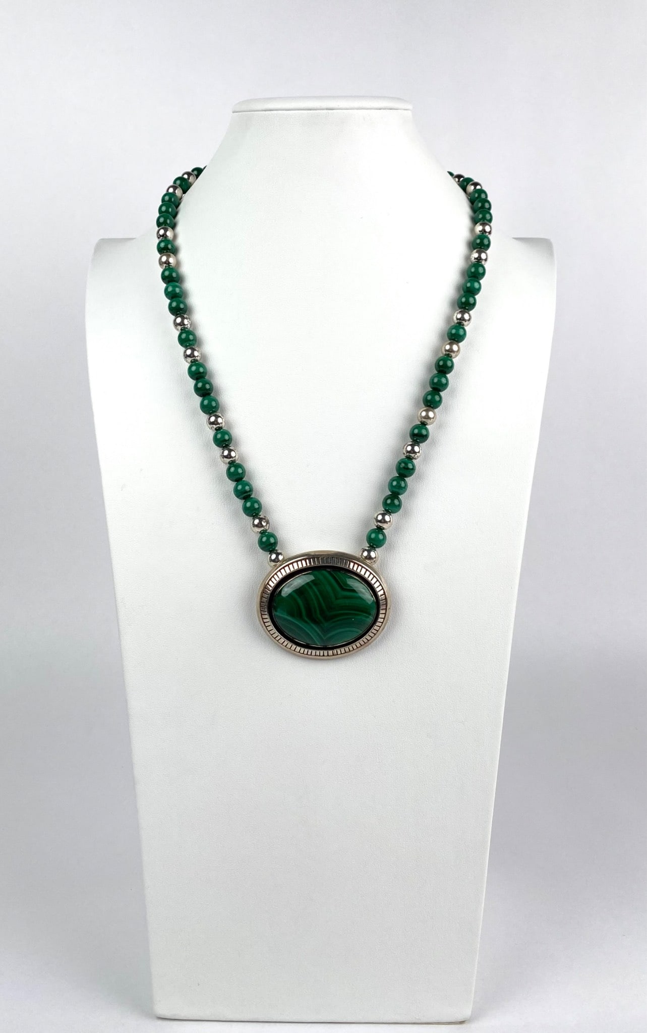 Native American Sterling Silver and Malachite Necklace: Sterling silver and malachite bead necklace featuring a polished oval malachite pendant surrounded by a detailed sterling silver bezel. The necklace incorporates alternating malachite beads and sterli