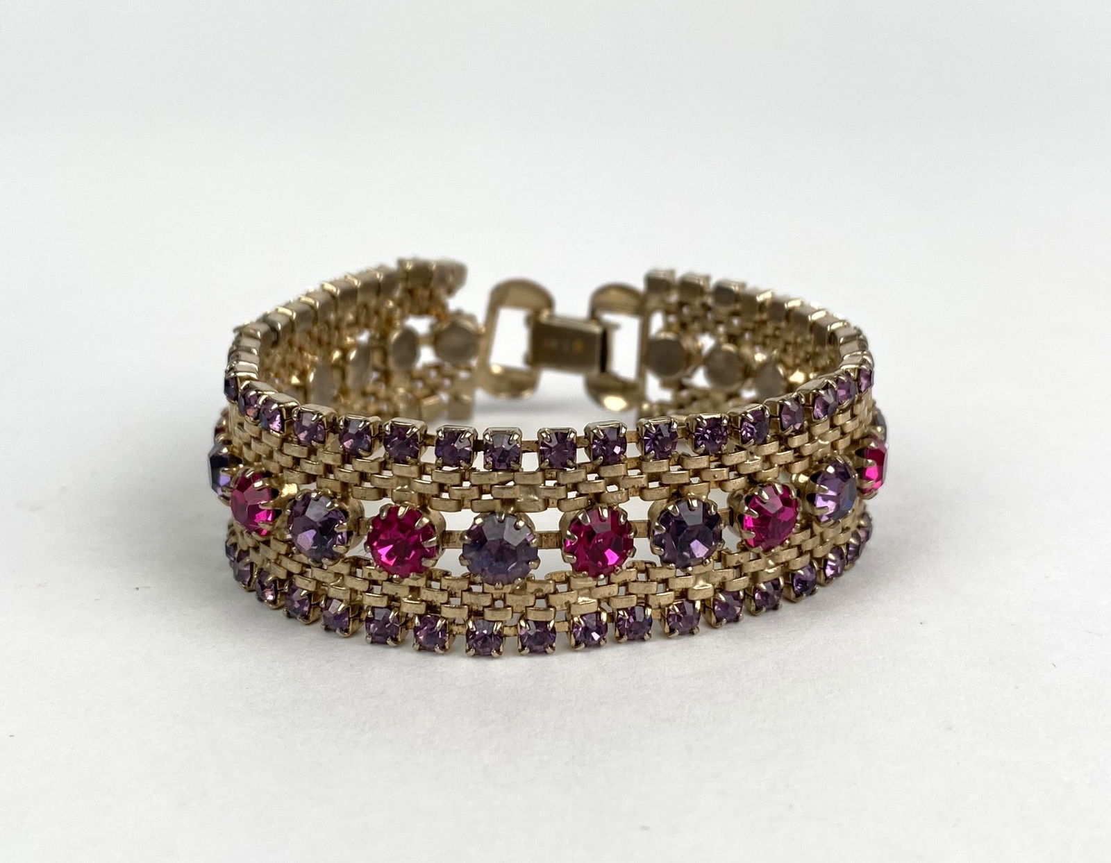 Weiss Gold Tone Bracelet with Pink and Purple Rhinestones: Gold-tone bracelet featuring alternating pink and purple rhinestones set across three rows. The bracelet is secured with a fold over clasp, marked Weiss on the underside. The piece exhibits detailed c