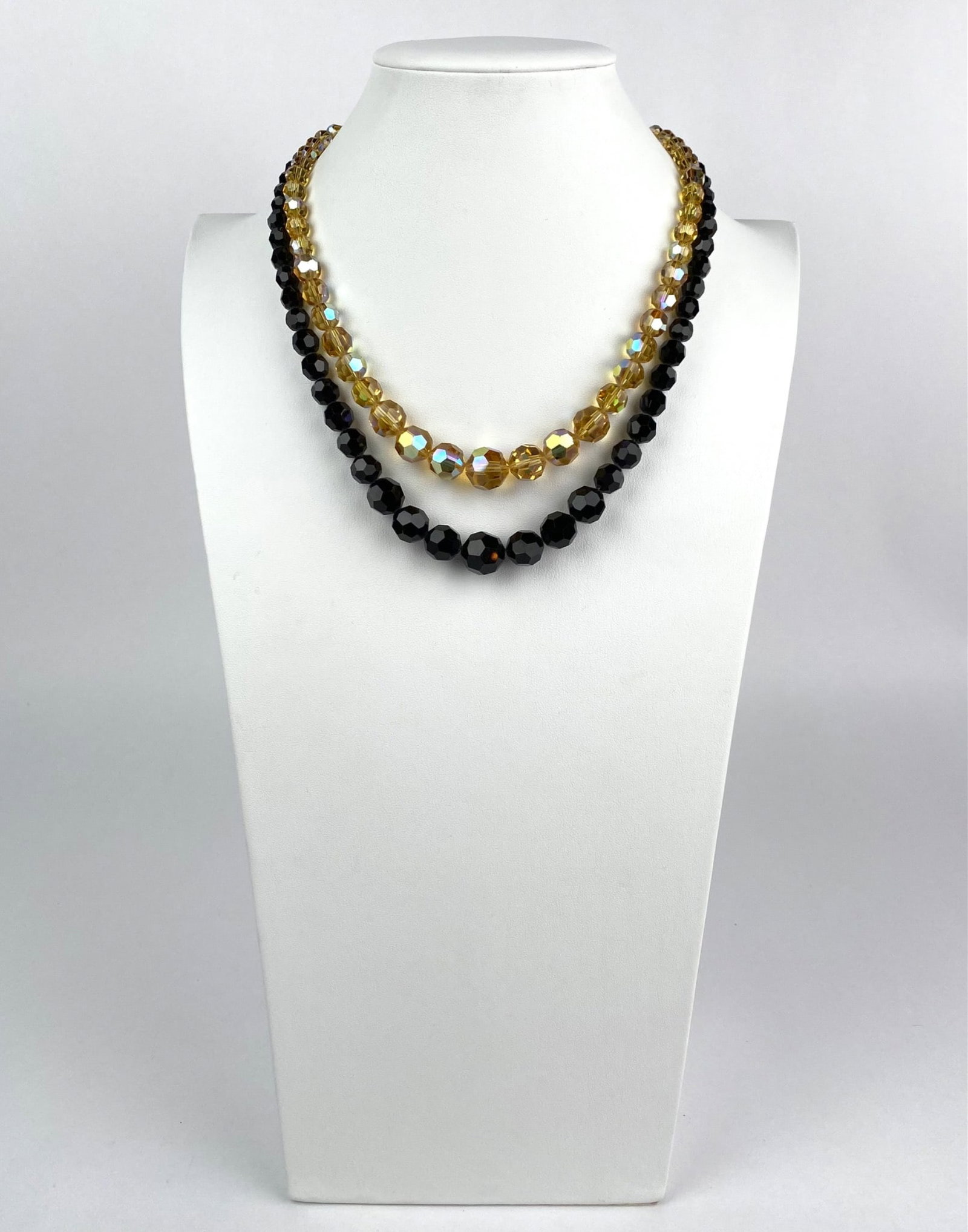 Vintage Double Strand Crystal Necklace: Double strand necklace featuring faceted black and amber toned crystals, with some amber crystals displaying an iridescent finish. The necklace is secured with a gold tone rectangular clasp adorned wi