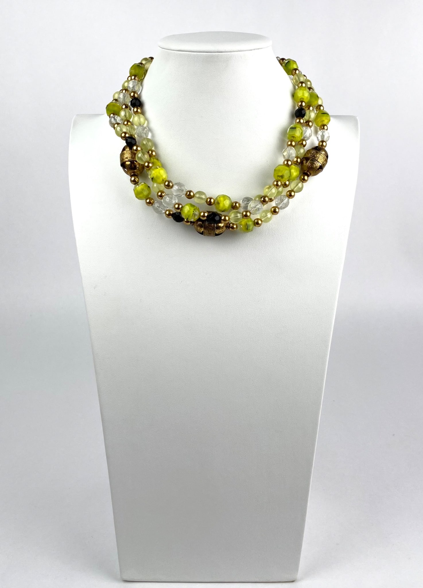 Multistrand Necklace with Green, Clear, and Gold Beads: Multistrand necklace comprising green, clear, and gold beads, accented with ornate gold toned decorative elements. Features a secure clasp. Materials include glass and metallic beads. In good conditio