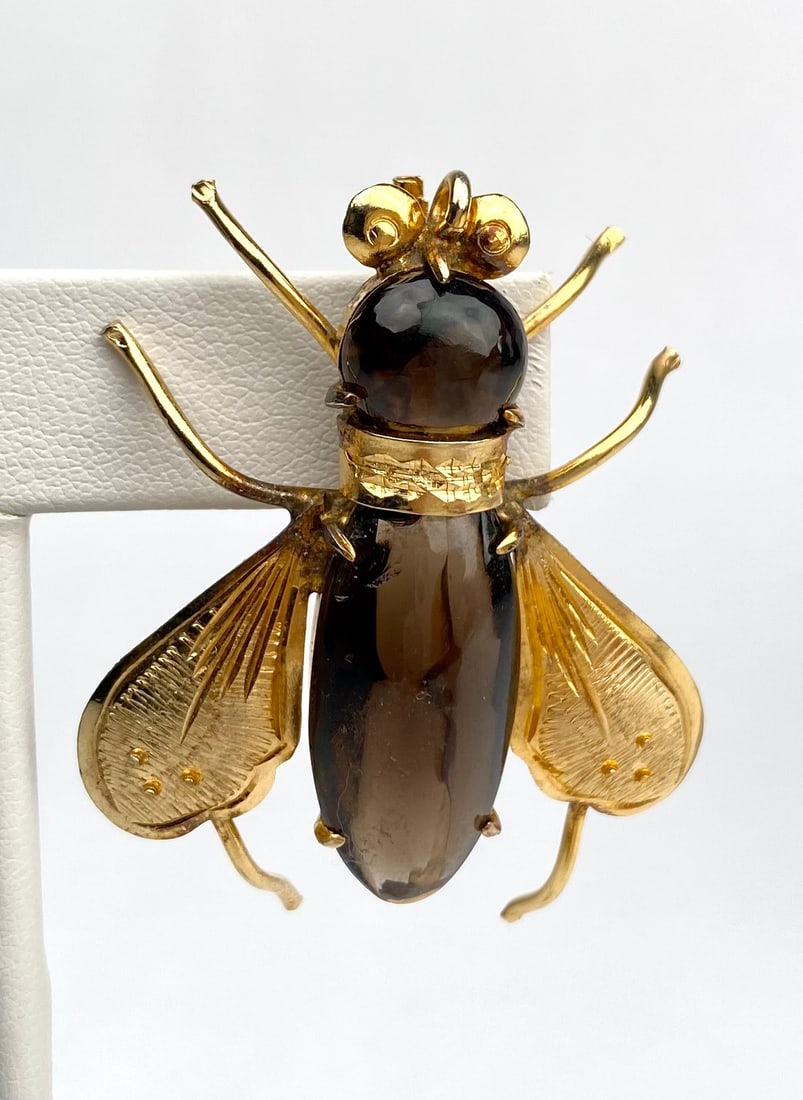 Gold Tone Smoky Glass Fly Brooch: Gold Tone brooch designed in the form of a bee or fly, featuring smoky glass style elements used for the body and head. The wings and legs are intricately crafted in a yellow gold tone metal. It featu