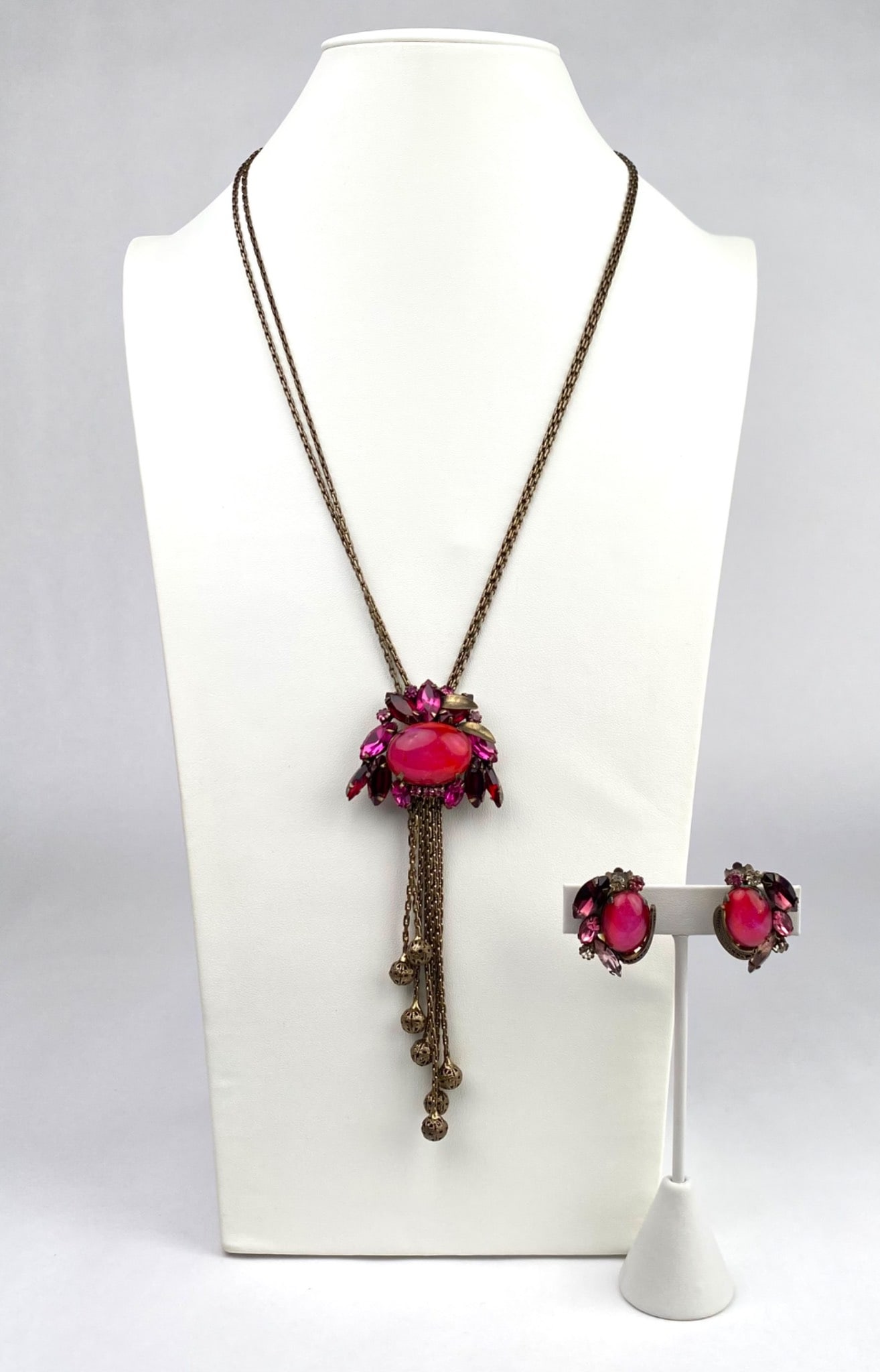 Vintage Pink Stone and Brass Necklace and Earring Set: Necklace and clip on earring set consisting of a brass tone metal with pink glass stones in varying cuts, including marquise and cabochon styles. The necklace features a pendant with cascading chains 