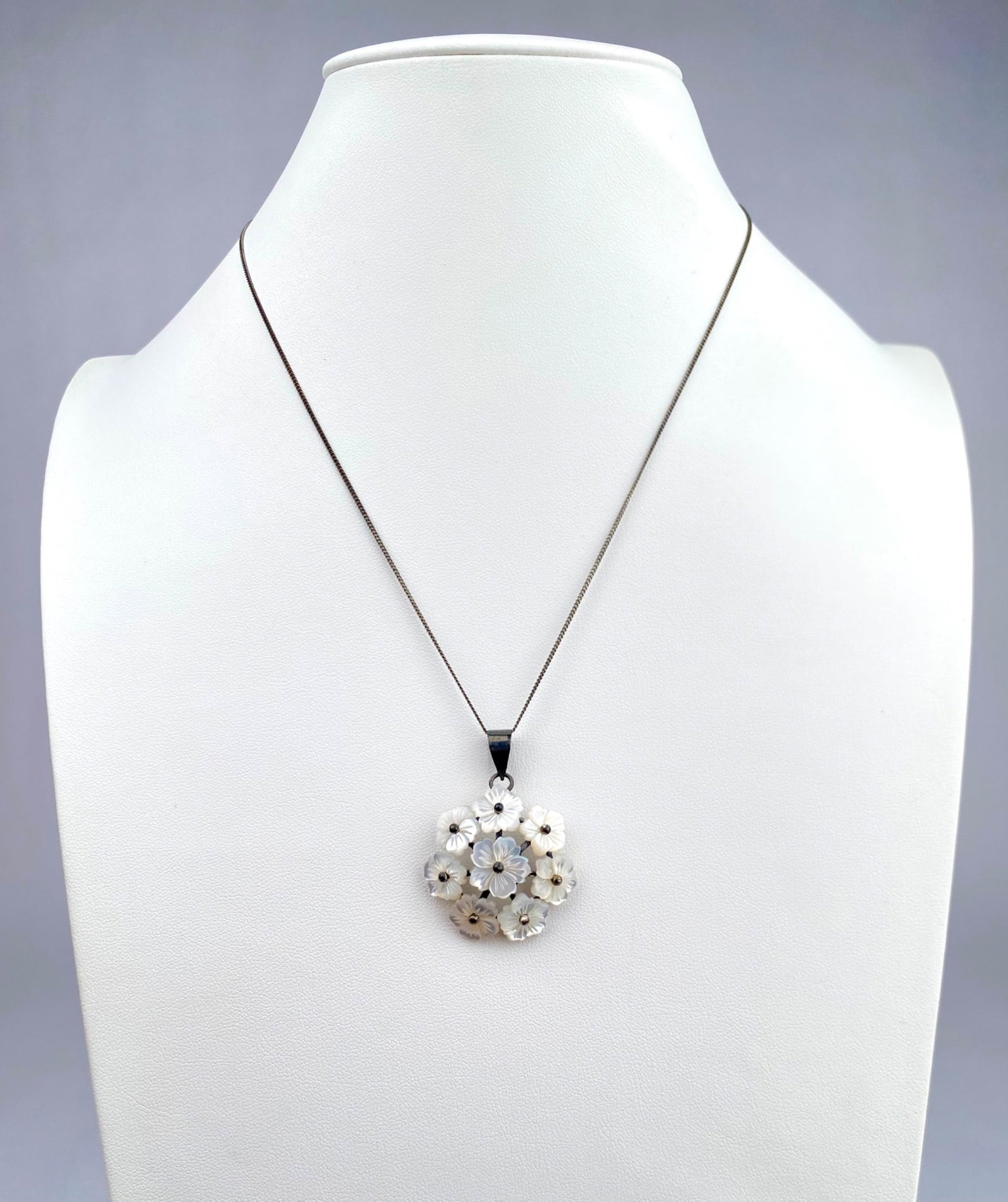 Sterling Silver Necklace with Mother of Pearl Flower Pendant: Sterling silver necklace featuring a floral pendant crafted from mother of pearl floral components. The pendant comprises intricately arranged flowers with small silver tone accents in the center. The