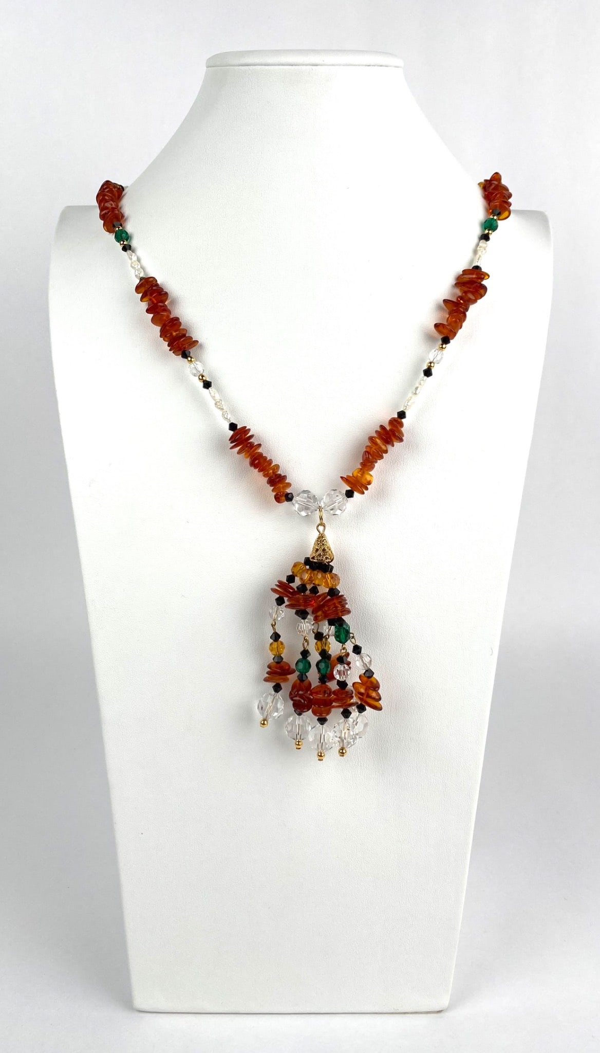 Amber and Crystal Drop Necklace with Gold Tone Accents: Amber, crystal, and bead necklace featuring gold tone accents and a multi strand pendant drop. The necklace has irregularly shaped amber beads, clear and green faceted beads, and black spacers. It is