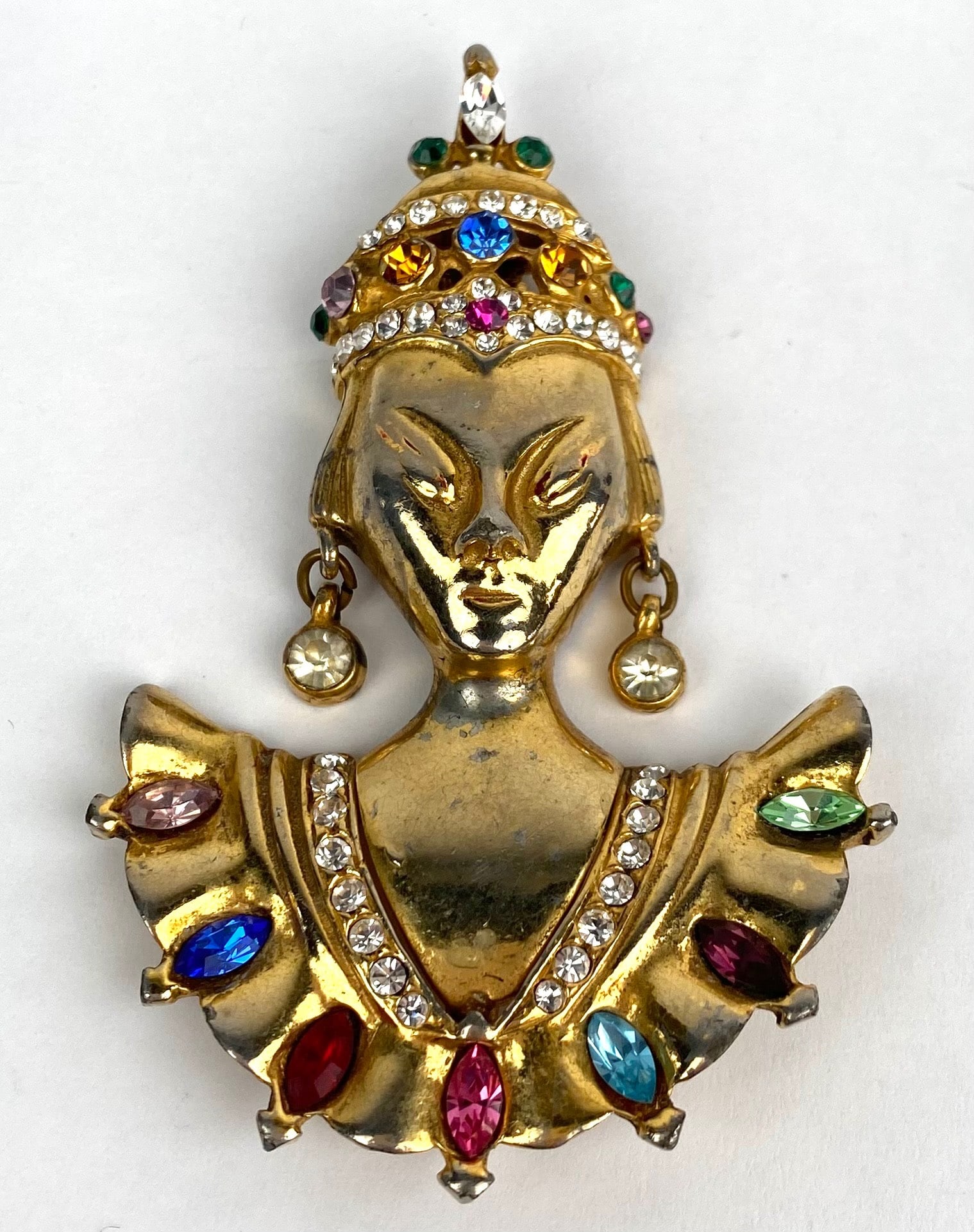 Reinad Gold Tone Figural Brooch with Multicolor Rhinestones: Reinad figural brooch in a gold tone finish. Features a decorative figure adorned with multicolor rhinestones and clear crystal accents, with a detailed headdress and drop earrings. The reverse side i
