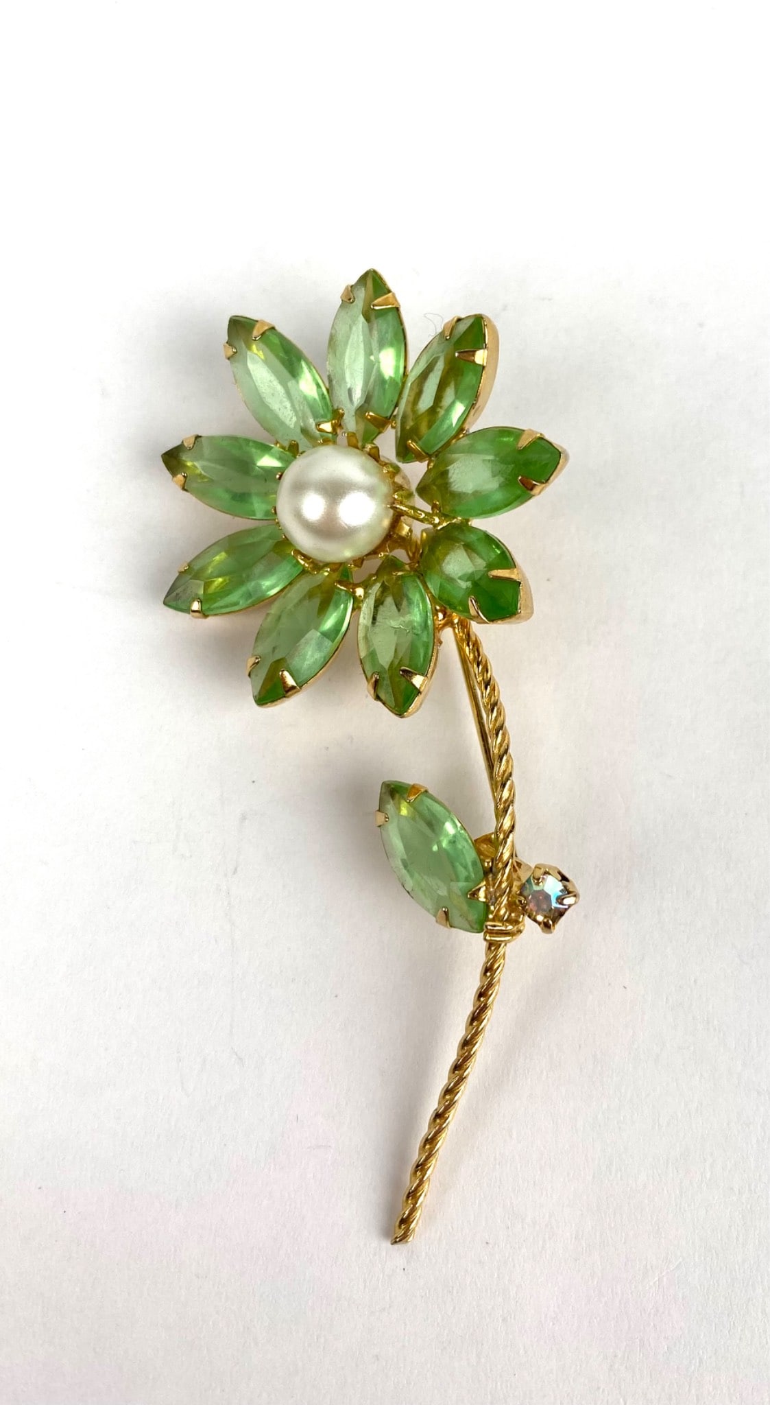 Gold Toned Brooch with Green Gemstone Petals, and Faux Pearl: Gold-toned brooch featuring green marquise-shaped gemstone petals arranged around a faux pearl centerpiece. Accented with a single rhinestone on the stem, which is styled with a twisted rope design. S