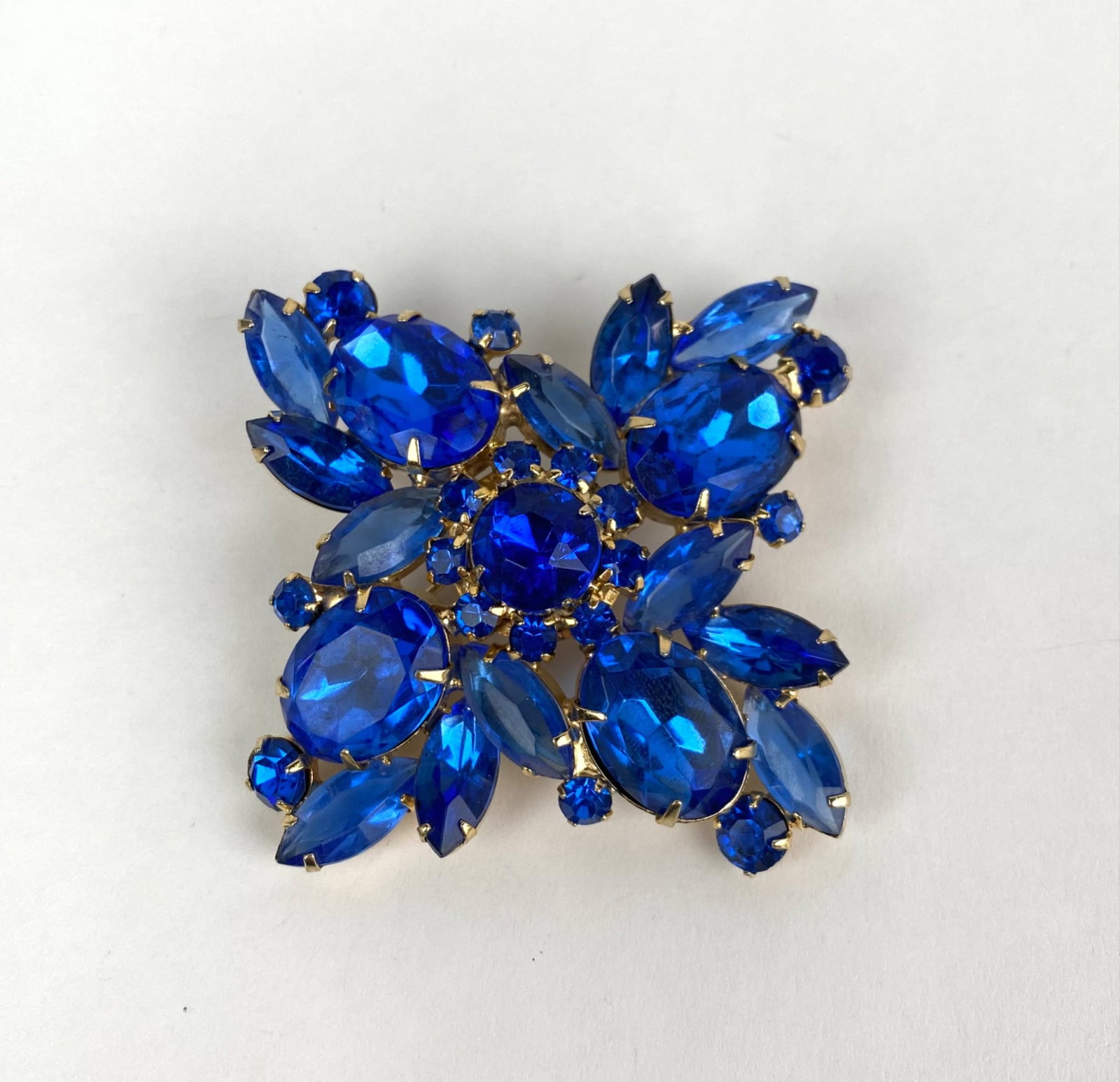 Gold Tone and Blue Rhinestone Floral Brooch: Gold tone floral brooch set with various blue rhinestones in round and marquise cuts. Features a secure pin back closure. In good condition with signs of wear consistent with age and use. Please see p