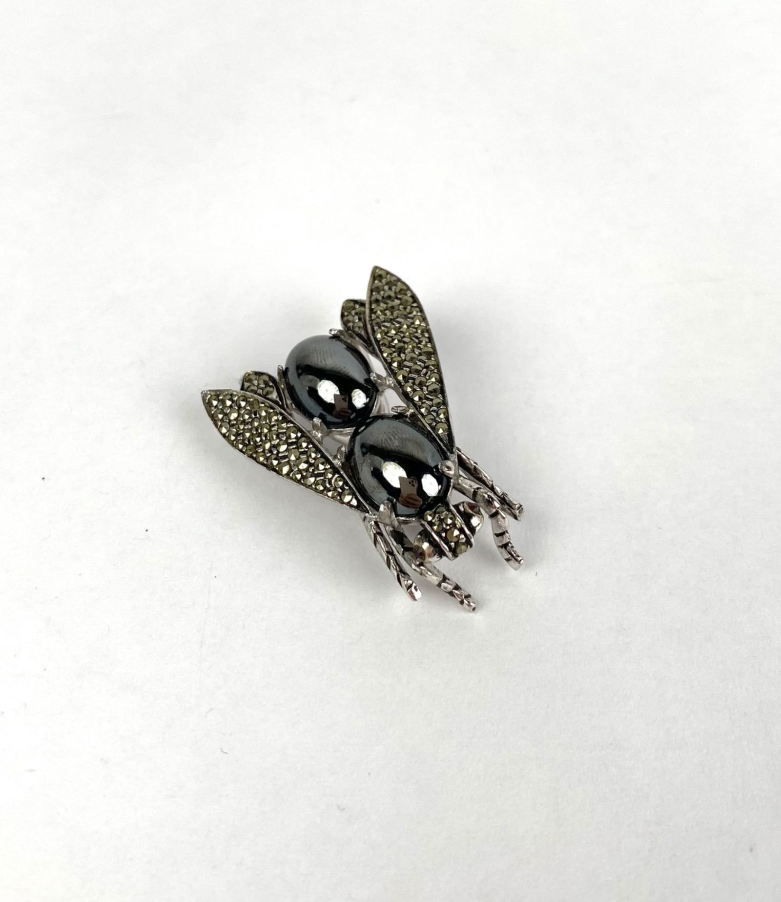 Silver Toned Fly Brooch with Marcasite Details Vogue JRLY: Sterling silver fly shaped brooch featuring hematite accents for the body and marcasite settings on the wings. Marked Vogue JLRY on the reverse. The design includes a secure pin clasp on the underside