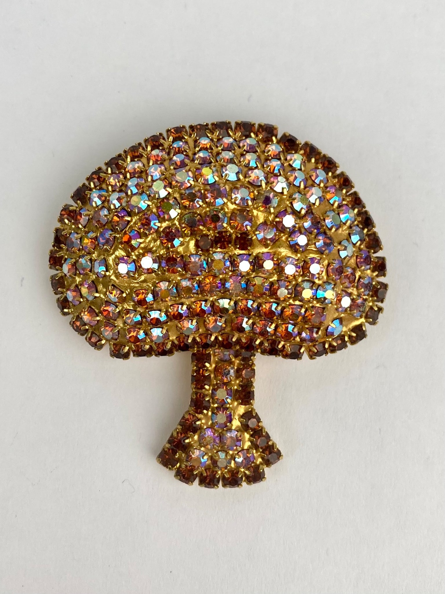 Vintage Basket Motif Brooch with Aurora Borealis Rhinestones: A gold-tone brooch featuring a basket-like design encrusted with aurora borealis rhinestones that emit multi colored iridescence. The back reveals a textured gold tone finish and a functional pin clas