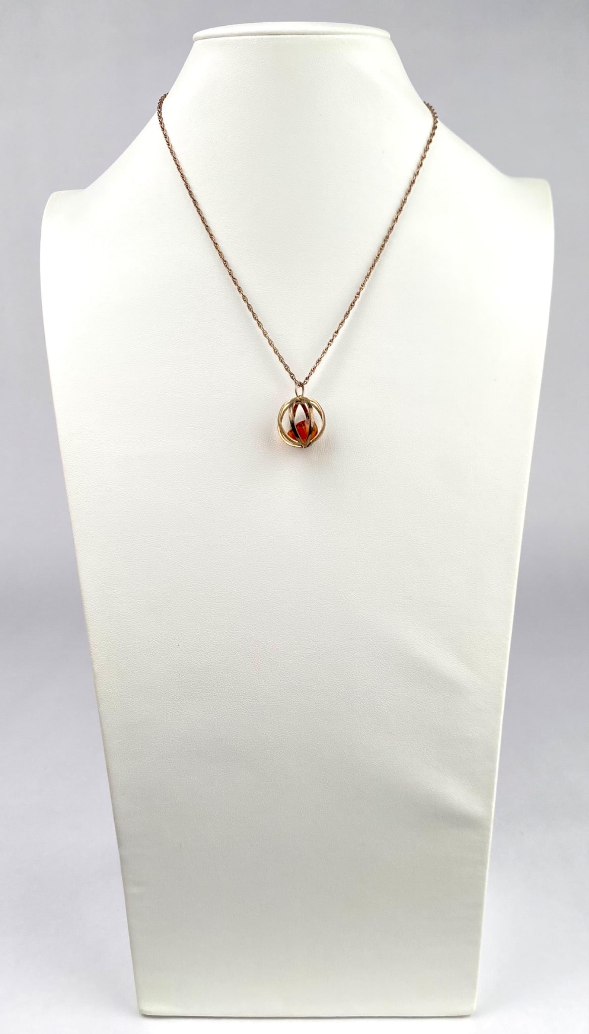 Sterling Silver and Amber Sphere Pendant Necklace: A sterling silver pendant necklace featuring a spherical pendant with an amber stone enclosed within an open frame design. The chain is crafted from sterling silver, as indicated by the STERLING mark 