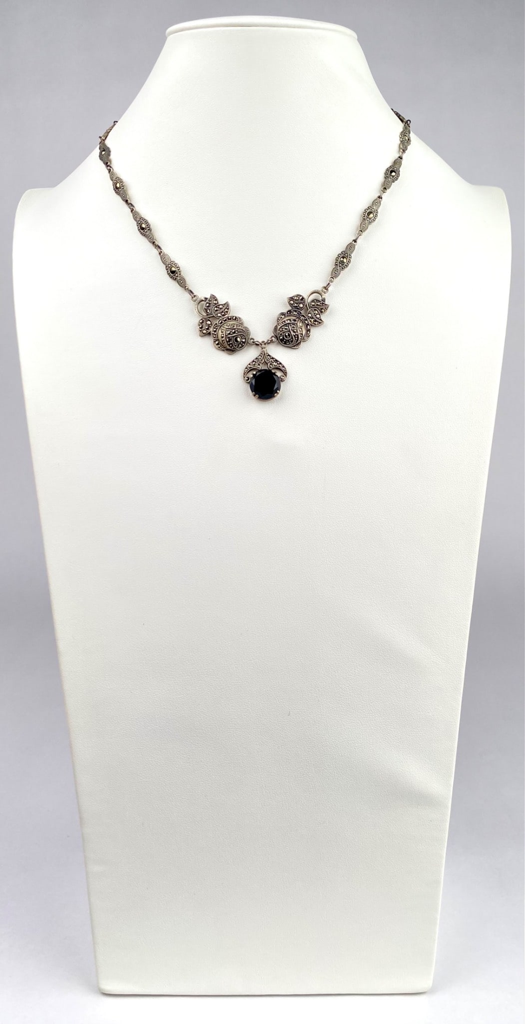 Sterling Silver Necklace with Onyx and Marcasite Accents: Sterling silver necklace featuring an ornate design with marcasite embellishments and a central black stone in a prong setting. The pendant is attached to a chain with intricate marcasite accented lin