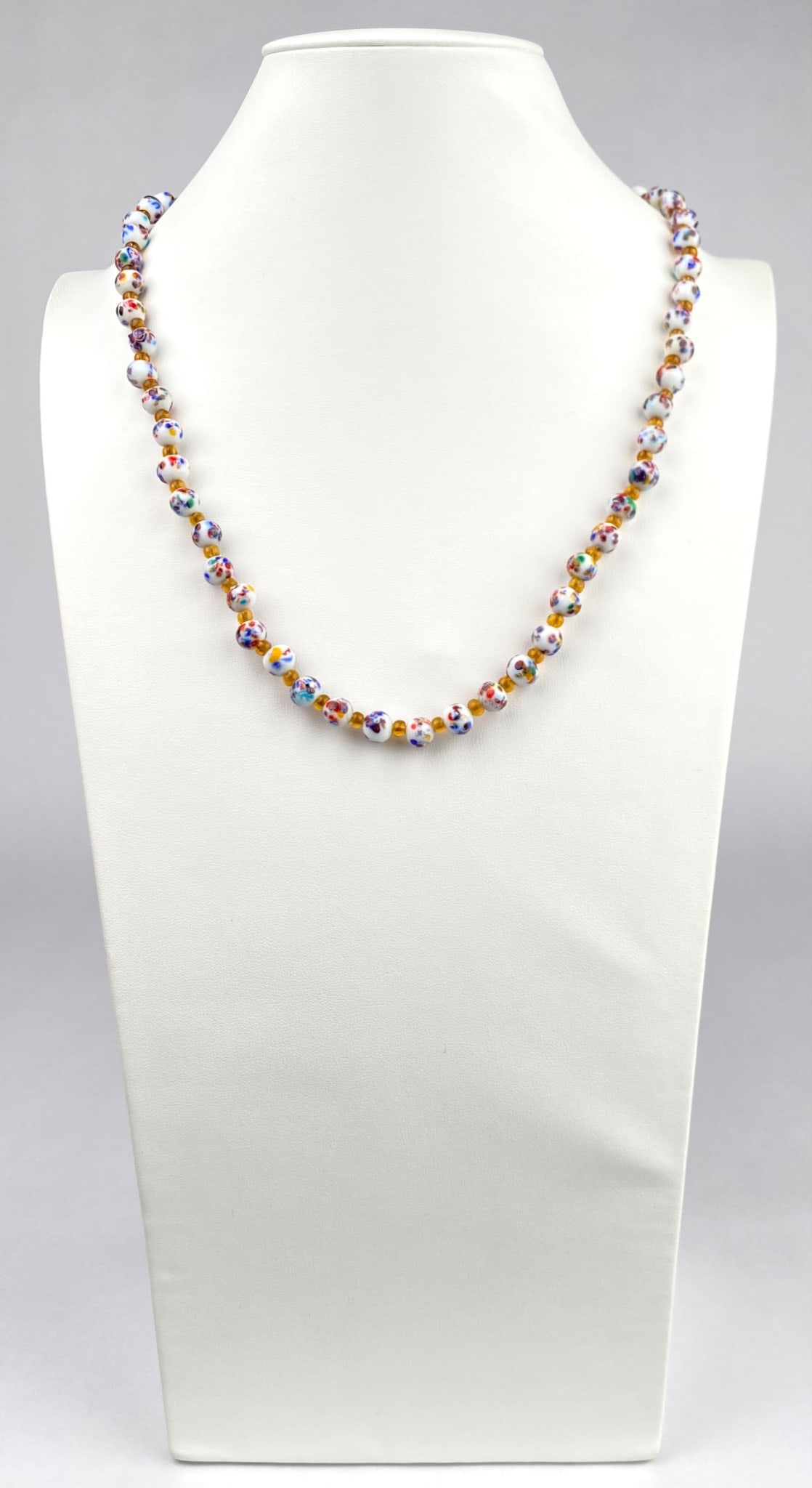 Multicolored Murano Glass Beaded Necklace With Barrel Clasp: Multicolored glass beaded necklace featuring white beads with intricate multicolored designs interspersed with yellow spacer beads. Fitted with a brass barrel twist clasp for secure closure. Necklace