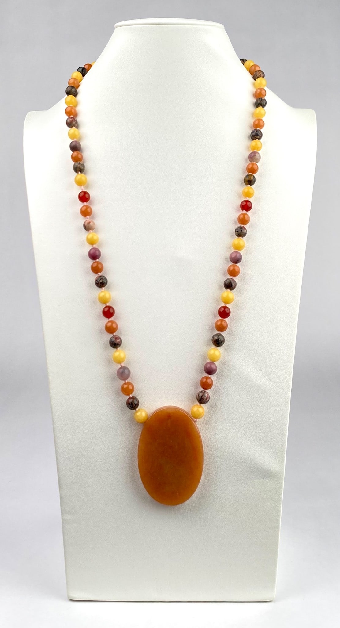 Multicolor Stone Beaded Necklace With Oval Pendant: A multicolor beaded necklace featuring spherical stone beads in warm tones of yellow, orange, red, and brown, complemented by an oval shaped orange hued pendant. The beads are strung on a secure threa