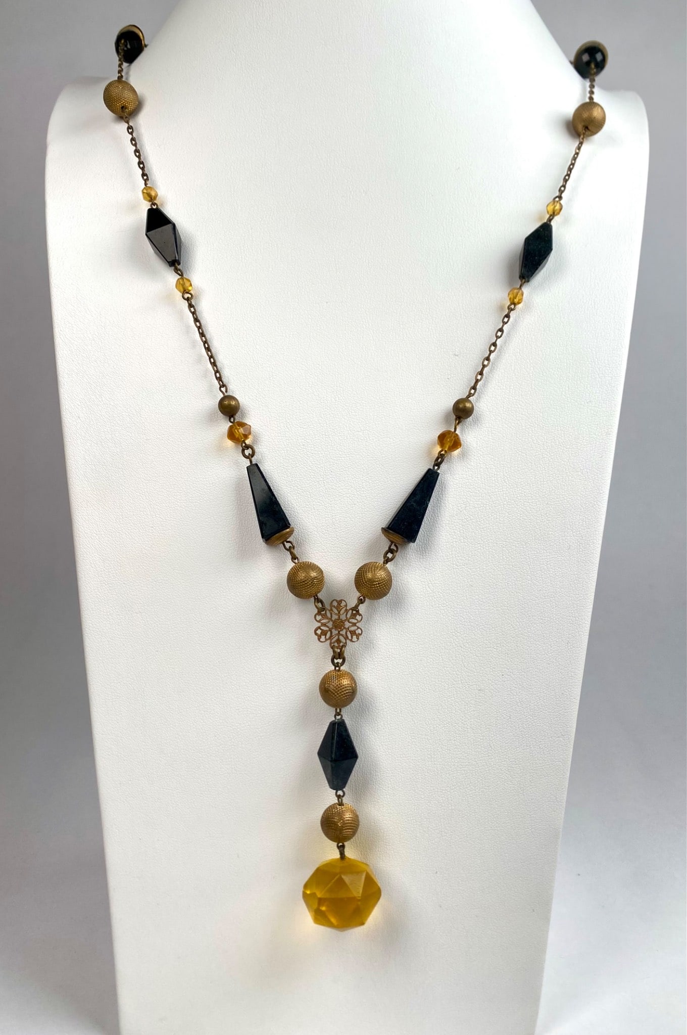 Black and Gold Tone Glass Bead Necklace with Yellow Pendant: Black and gold tone beaded necklace featuring faceted glass beads in varying shapes and textured gold tone elements. Designed with a prominent faceted yellow glass pendant suspended from gold tone com