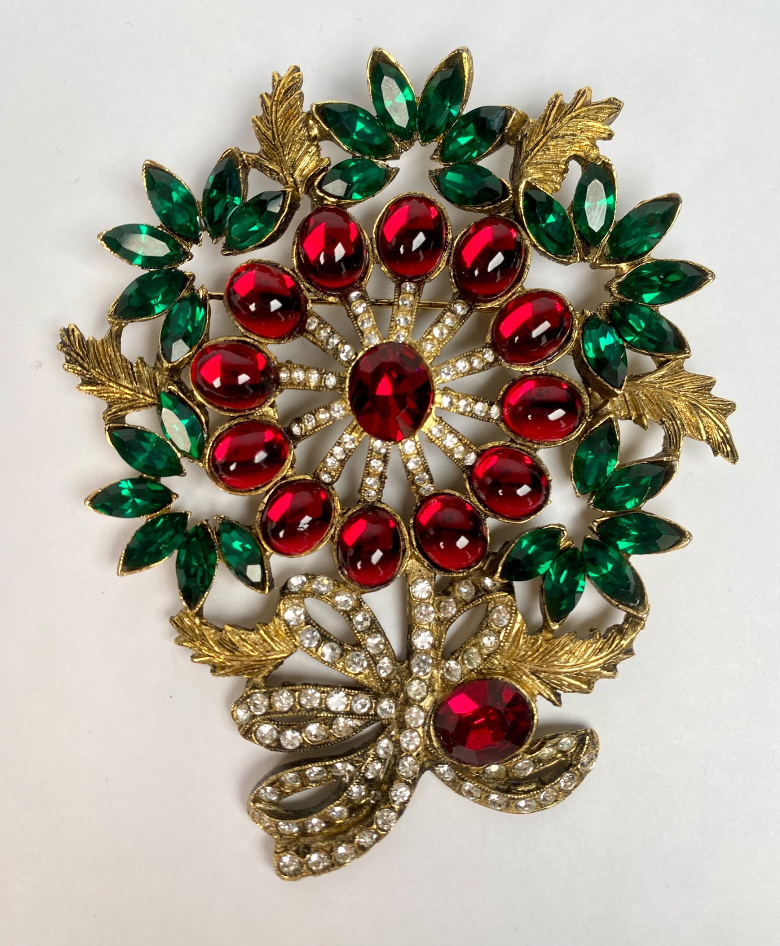Costume Jewelry Brooch With Red and Green Stones: A gold tone brooch featuring red oval and marquise cut stones, green marquise cut stones, and rhinestone accents in a floral arrangement. The reverse side reveals a textured gold-tone surface with a f