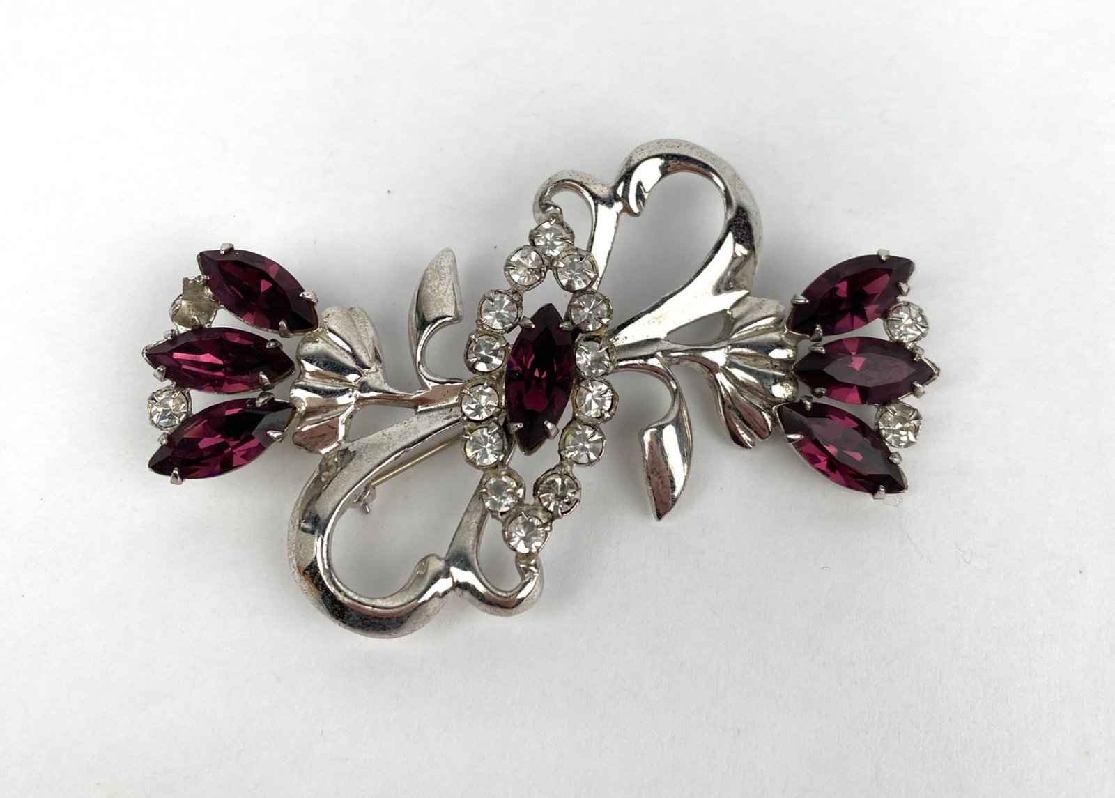 Sterling Silver Brooch with Purple and Clear Gemstone Accents: Sterling silver brooch featuring an intricate floral design adorned with purple marquise cut gemstones and clear round accents. The back is stamped STERLING. In good condition. Please see photos for a