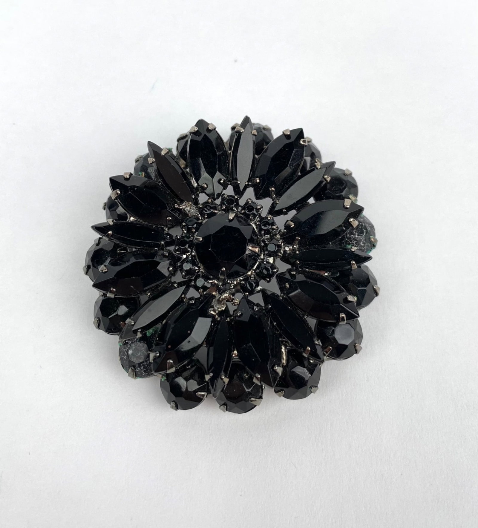Vintage Costume Jewelry Black Rhinestone Brooch: Black glass rhinestone floral brooch featuring layered and faceted stones arranged in a circular floral pattern. Set in a metal base with a secure pin mechanism on the reverse side. In good condition 