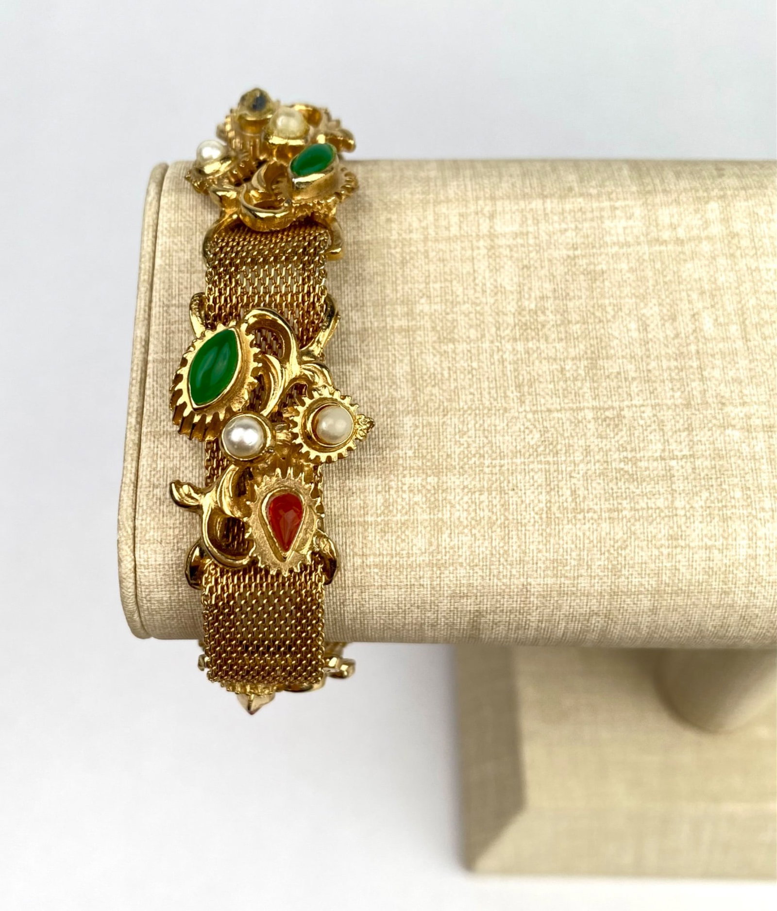 Victorian Mesh Bracelet With Faux Gemstone and Pearl Accents: A gold tone mesh bracelet featuring decorative elements with faux pearl and cabochon style gem accents in green and red tones. The bracelet features a detailed clasp and intricate ornamental designs a