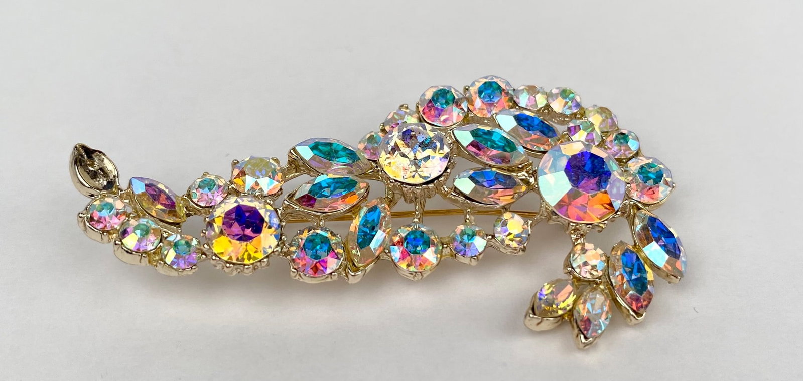 Vintage Aurora Borealis Rhinestone Brooch: Silver tone brooch embellished with multi faceted aurora borealis rhinestones in various sizes, arranged in a flowing, organic pattern. The brooch features a secure pin clasp on the reverse. One rhine
