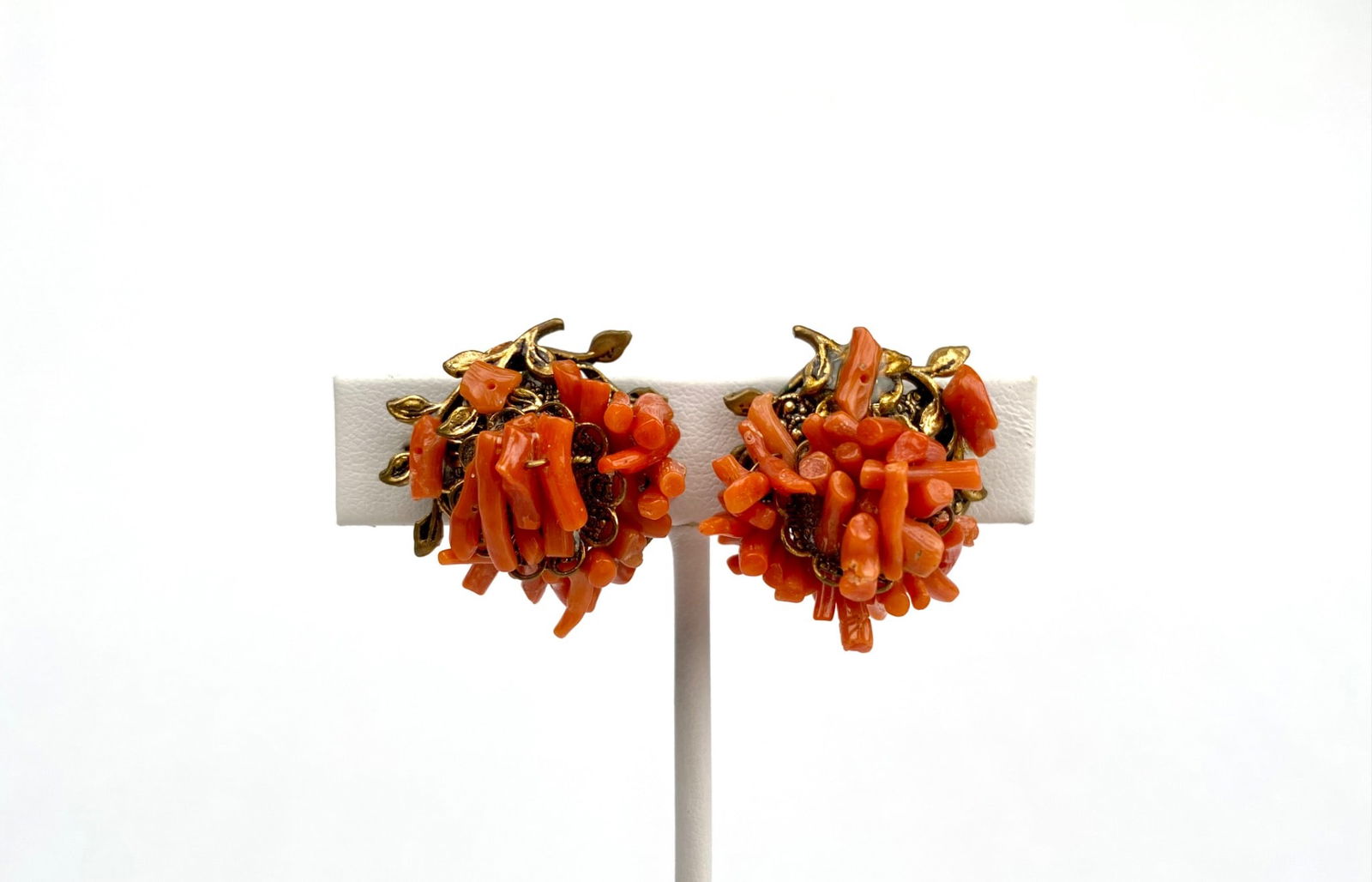 Pair of Brass and Coral Cluster Clip Earrings: Pair of brass toned clip on earrings featuring orange coral branch clusters in a floral inspired design. The intricately crafted metal base has a decorative leaf motif, enhancing the natural appearanc