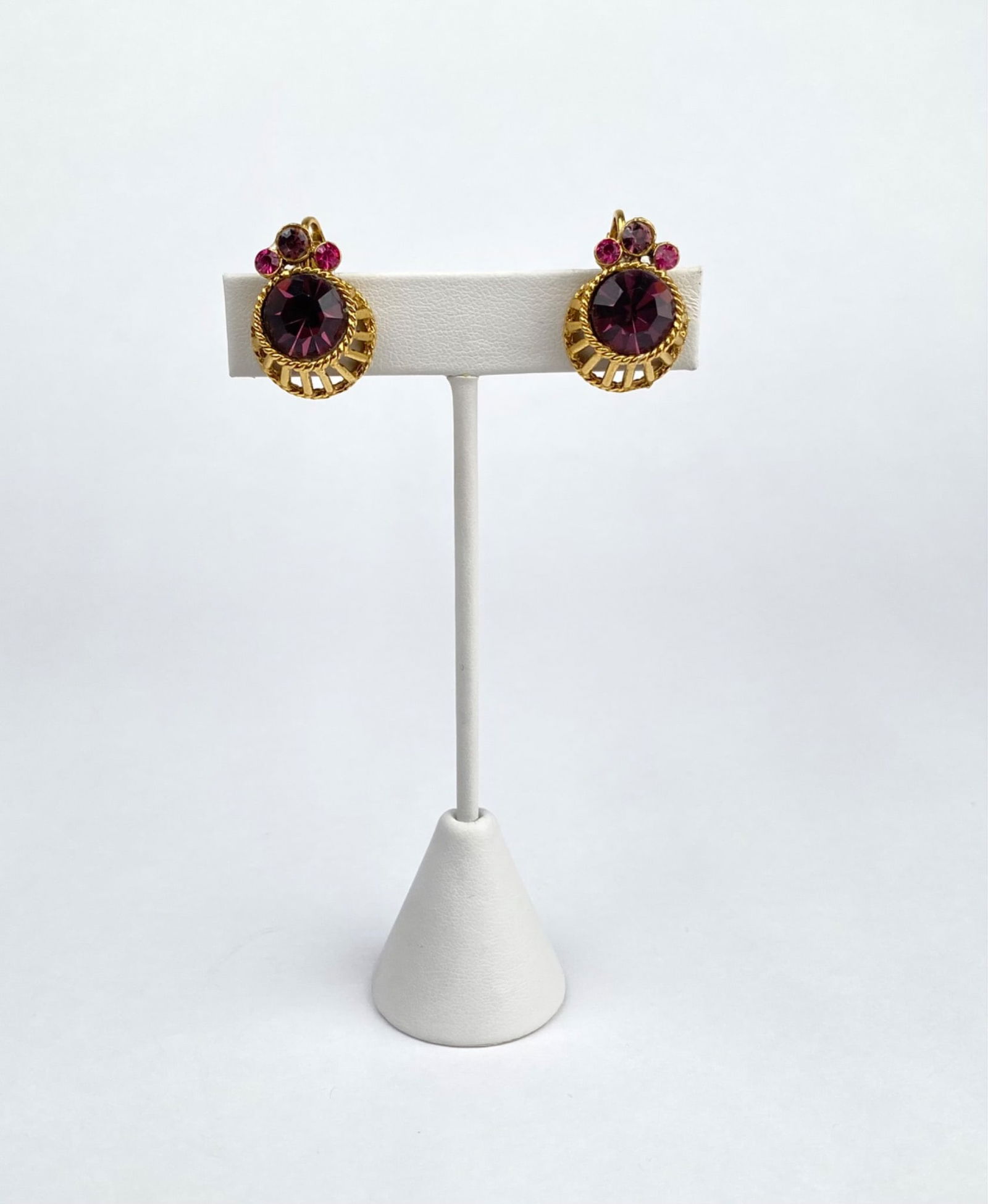 Mid Century Pink and Purple Rhinestone Clip On Earrings: Pair of gold tone clip on earrings featuring purple and pink stones in a circular design with intricate rope like and cutout details. Clip back closures for comfortable wear. Estimated to be from the