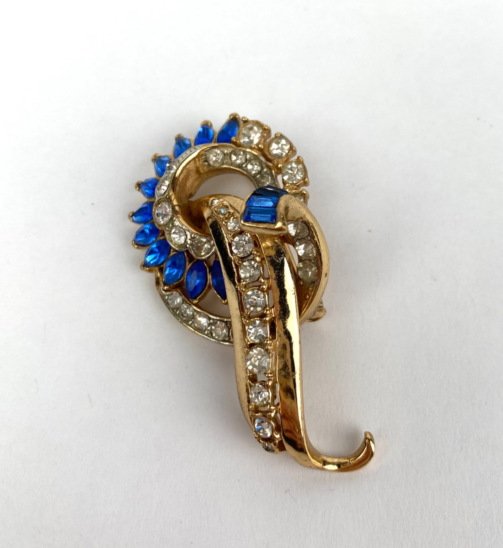 Coro Gold Tone Brooch with Blue and Clear Rhinestones: Coro gold tone brooch featuring a looped design adorned with blue and clear rhinestones. The brooch includes both baguette cut and marquise cut stones for added dimension. The reverse side is stamped
