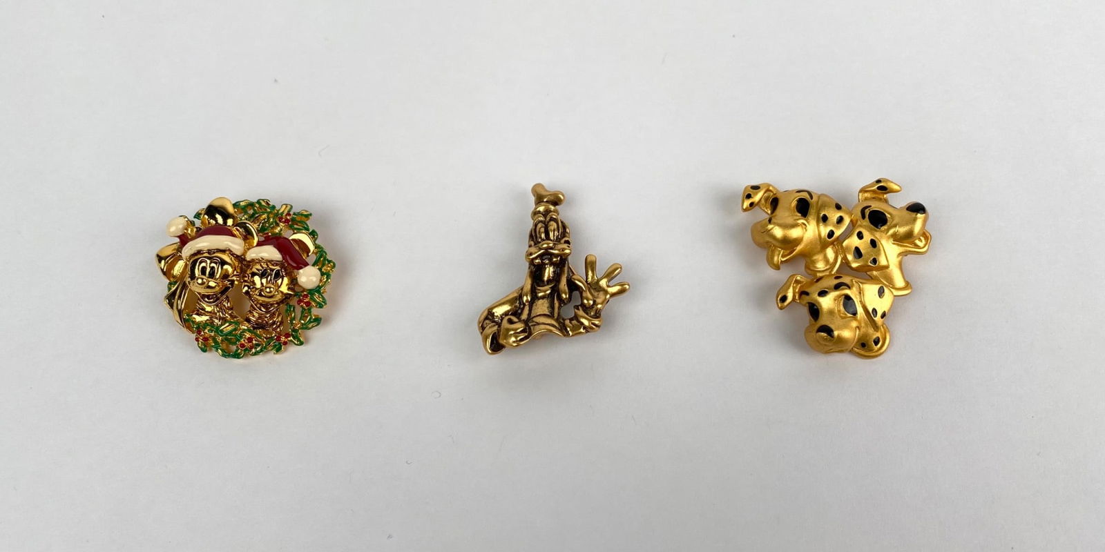Set of Three Gold Tone Disney Character Brooches: A set of three gold tone Disney themed brooches featuring beloved characters. Includes a wreath design with Mickey and Minnie Mouse in Santa hats, a brooch modeled after Goofy, and a brooch depicting