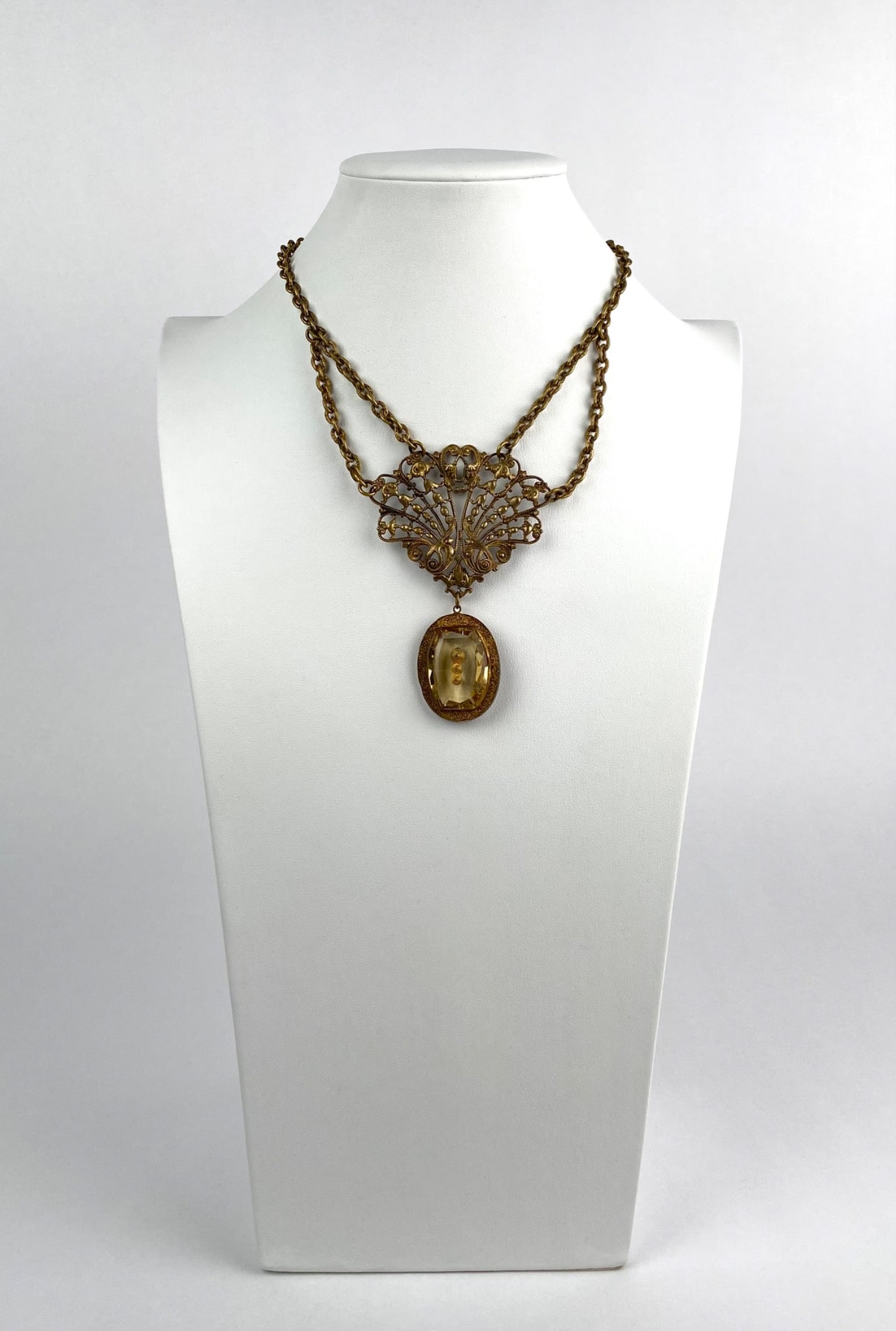 Ornate Costume Jewelry Necklace with Filigree Pendant: An intricately designed gold-tone necklace featuring a multi-chain construction with an ornate filigree pendant. The center of the pendant showcases a large oval citrine-colored drop accented with dec