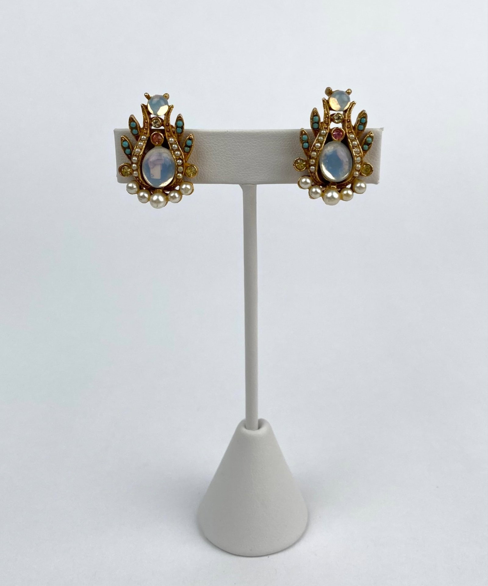Mode Art Indian Revival Clip On Earrings: Pair of ART signed gold tone clip on earrings featuring faux moonstones, turquoise bead accents, simulated pearls, and colored rhinestones in an ornate design. The earrings are marked ‘ART’ on the