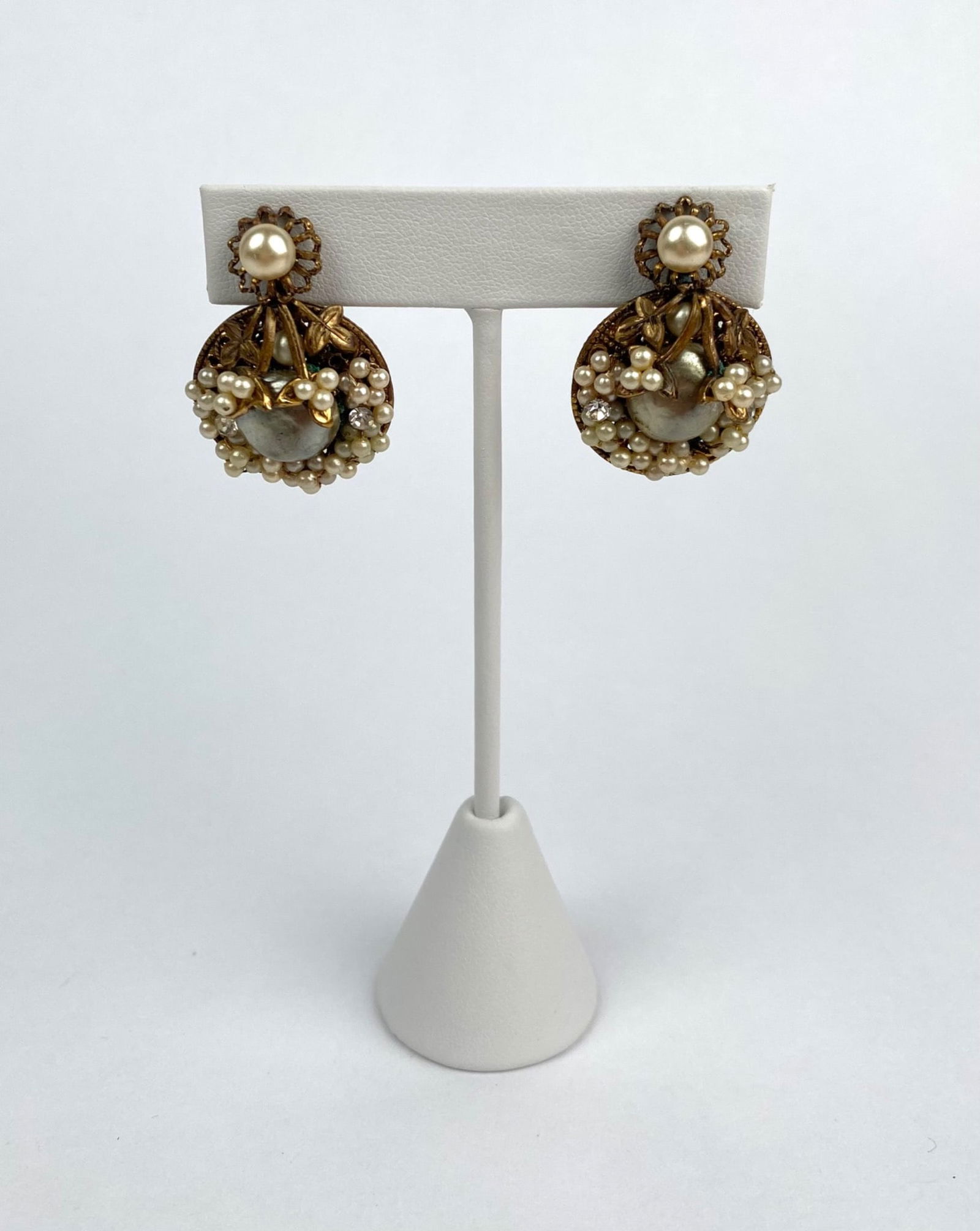 Mid Century Gold Tone Faux Pearl and Filigree Screw on Earrings: A pair of gold tone screw on earrings featuring intricate filigree backs and faux pearls. The design includes clusters of faux pearls surrounding a central cabochon style faux pearl, accented with flo
