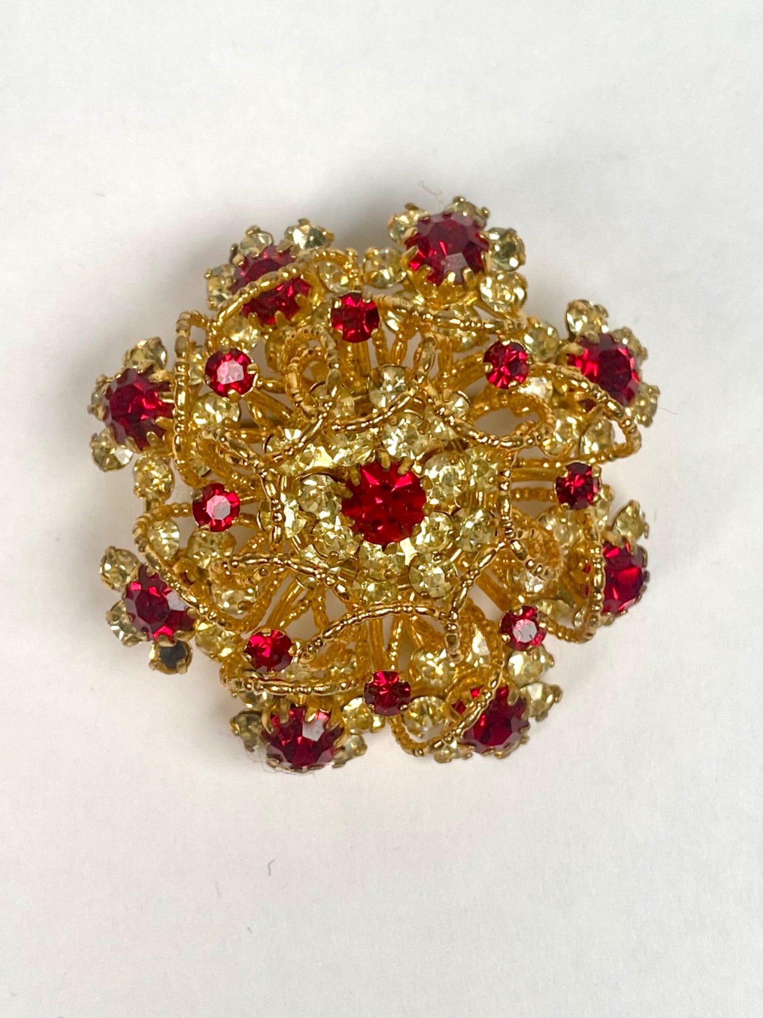 Austrian Costume Jewelry Brooch with Red and Yellow Rhinestones: A vintage Austrian gold tone metal brooch featuring ornate three dimensional filigree design adorned with red and yellow rhinestones in floral arrangements. Marked Austria on the reverse indicating th
