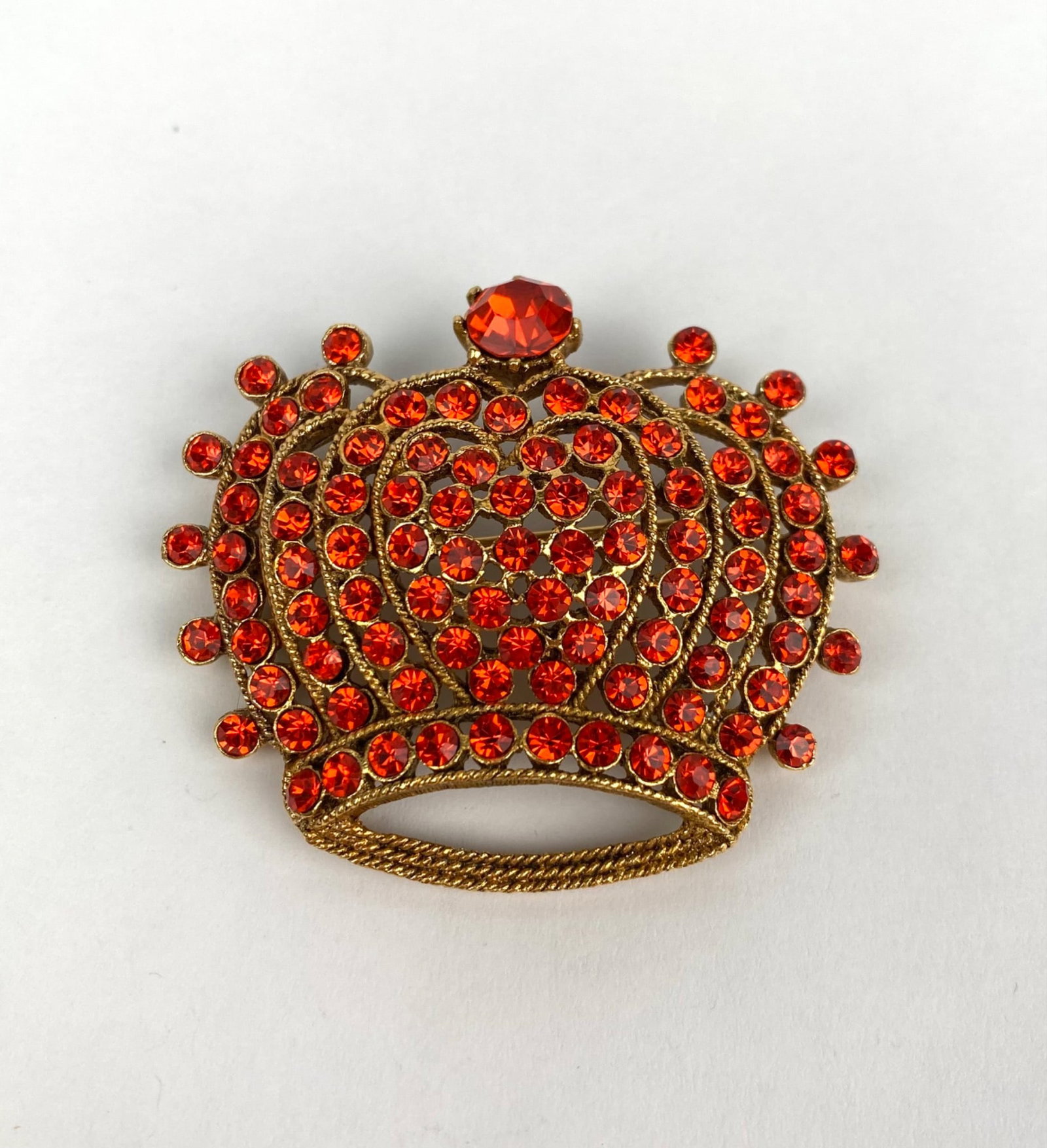 Mid Century Gold Tone Crown Brooch with Red Rhinestones: Gold-tone crown brooch adorned with vibrant red rhinestones in a tiered design. Features intricate metal detailing, a secure pin clasp on the back, and a bright central rhinestone. A fine example of v