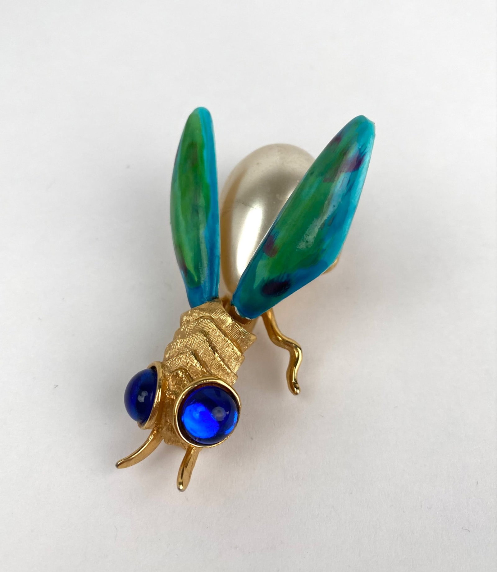 Mid Century Gold Tone Insect Brooch: Gold tone brooch in the design of an insect featuring a faux pearl body, enameled wings in green and blue hues, and glass elements for the eyes in vivid blue. Pin mechanism is functional. In good cond