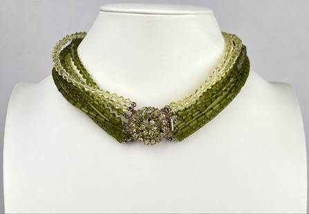 Mid Century Multi Strand Green and Clear Beaded Necklace: Multi strand necklace featuring alternating green and clear beads crafted from glass. The necklace showcases a round rhinestone encrusted clasp in green and clear tones, adding an elegant centerpiece.
