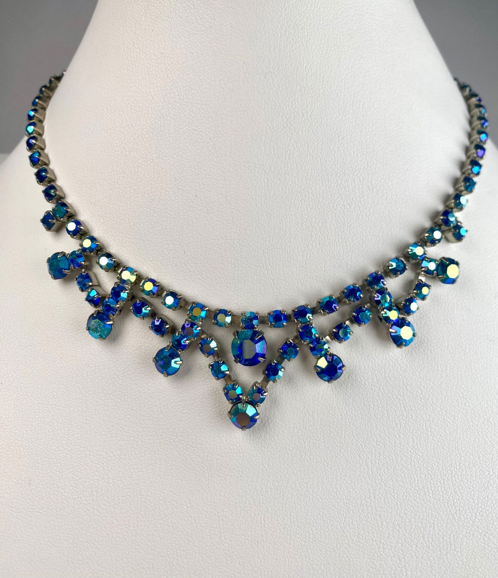 Juliana Aurora Borealis Rhinestone Necklace with Drop Design: A vintage necklace featuring vibrant blue aurora borealis rhinestones in a drop design. The necklace is constructed with faceted stones set in a silver tone metal frame, connected with a hook clasp fo