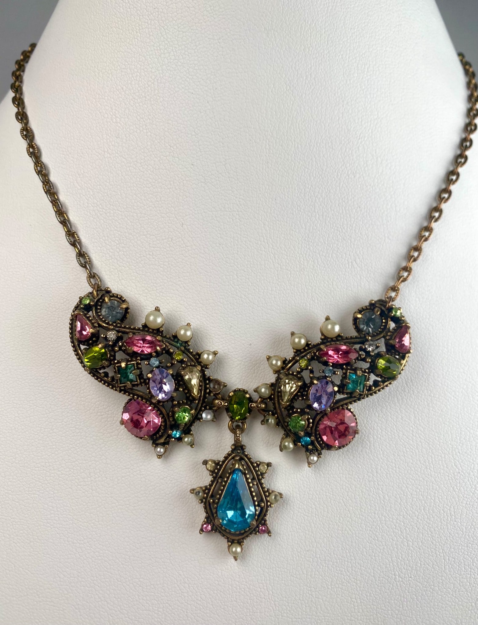 Czech Bohemian Export Necklace: Vintage statement necklace featuring a dazzling array of rhinestones in jewel tones of aqua, amethyst, rose and peridot, accented with small faux pearls and an ornate drop pendant. The design evokes a