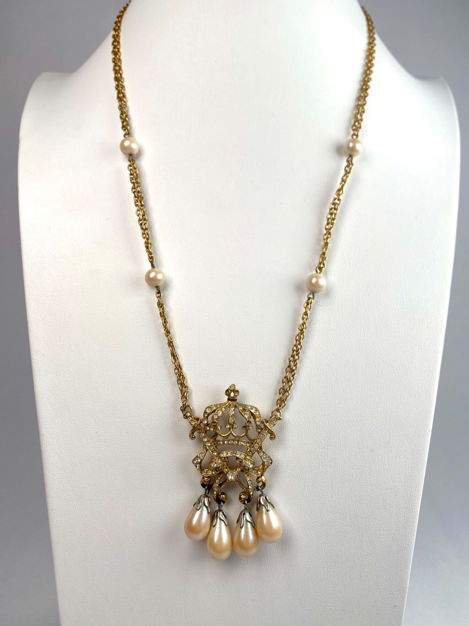 Baroque Revival Gold Tone Rhinestone Pendant Necklace: Gold tone necklace featuring an ornate crown like pendant adorned with sparkling rhinestones and four dangling faux pearl drops. The chain includes additional faux pearl accents and closes with a C-ri