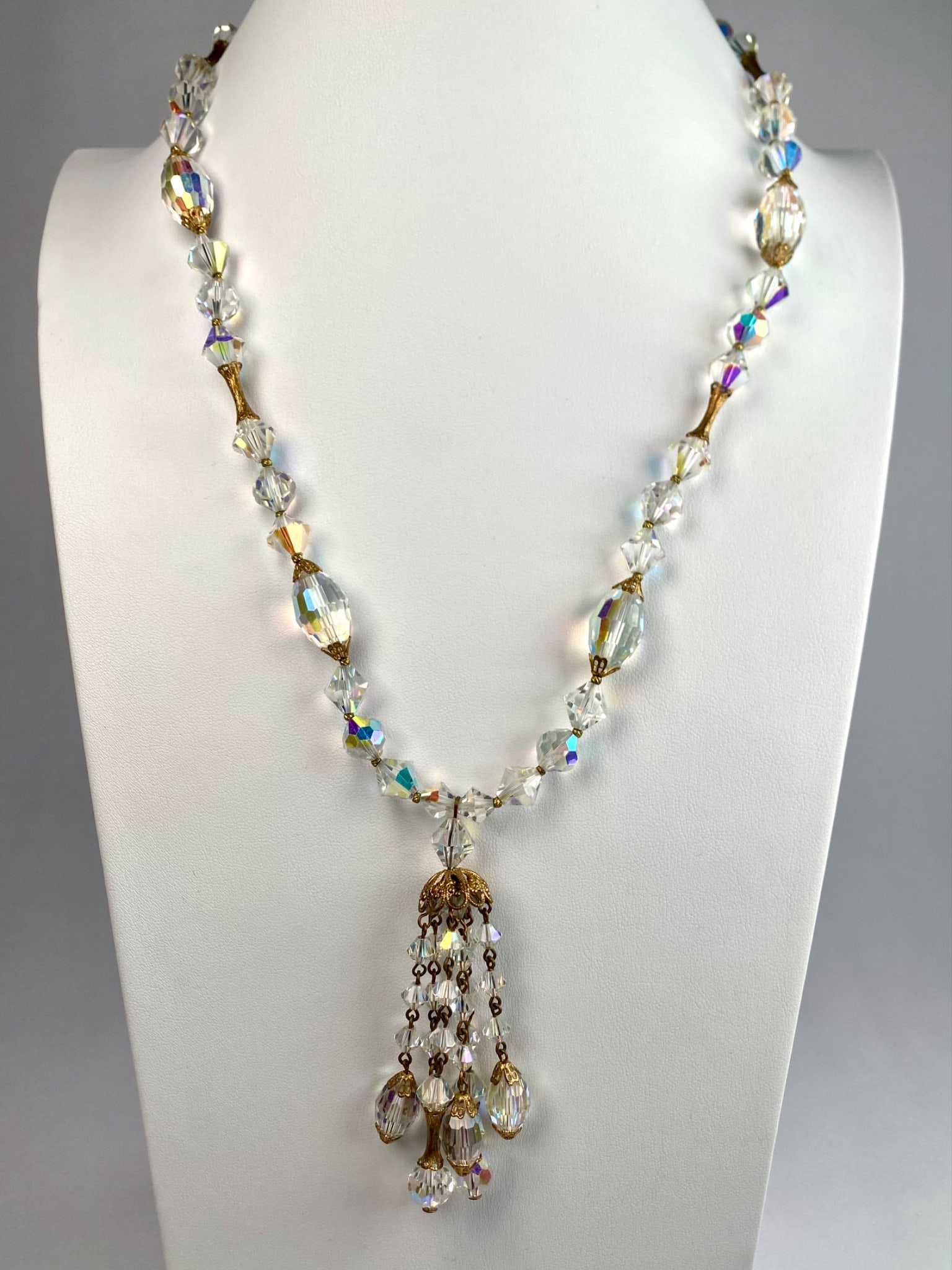 Aurora Borealis Crystal Necklace with Gold Tone Accents and Tassel Pendant: Aurora borealis crystal necklace features faceted beads and gold tone accents. The necklace includes a prominent tassel pendant with cascading crystal drops. Features a hook clasp for closure and an e